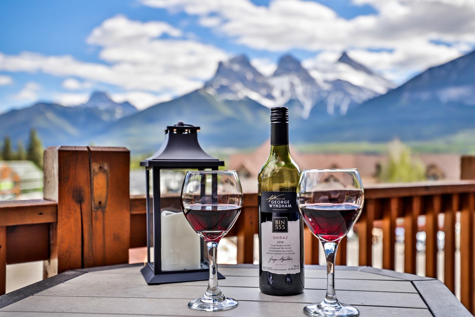 Wine bottle and two glasses of red wine on a table overlooking mountains.