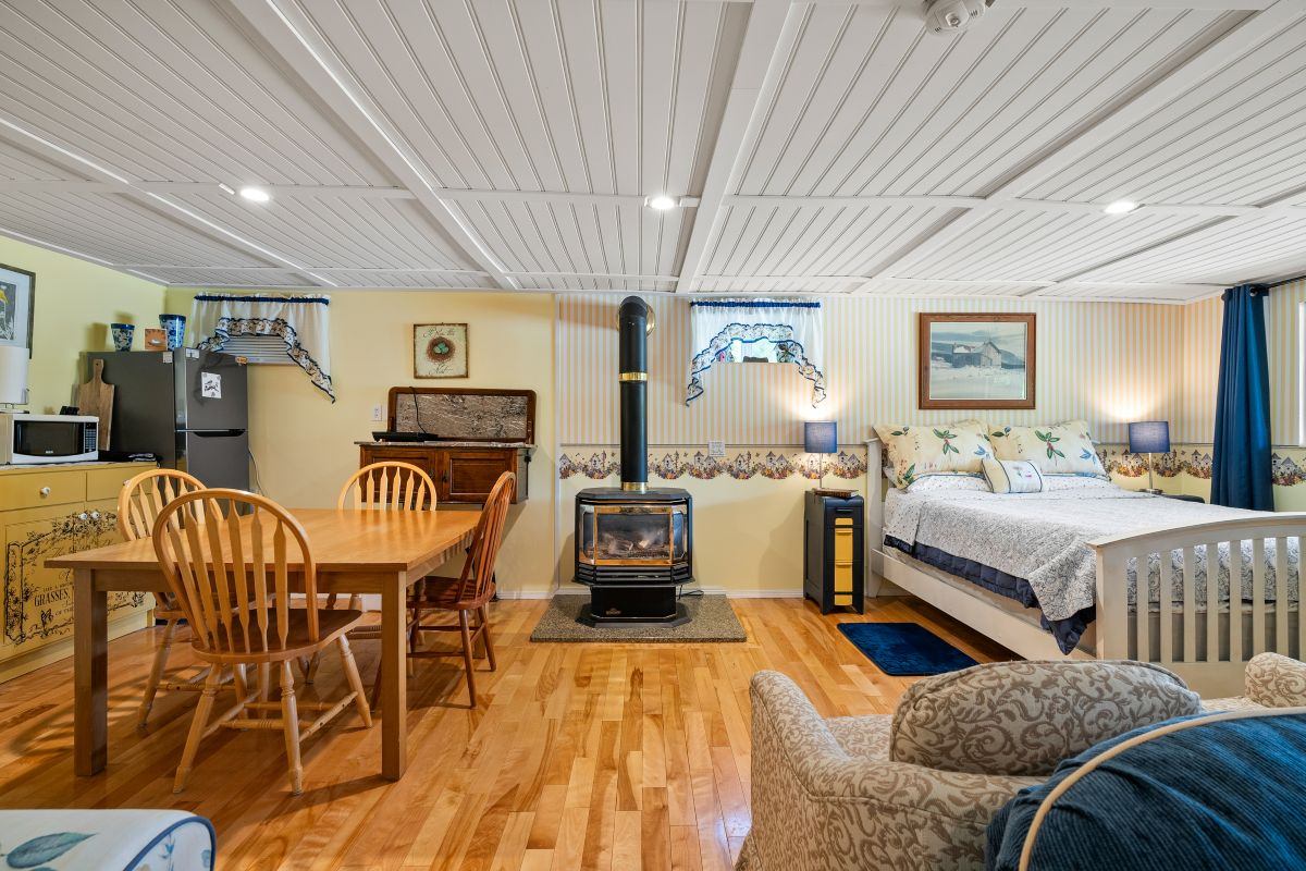 Open-plan space with dining table, bed, and wood stove on hardwood floors.