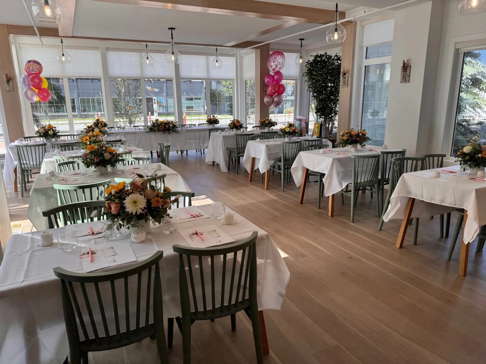 Sunlit event room with decorated tables, flower arrangements, and balloons