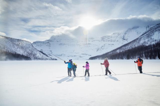 Family on a Tamarack Outdoors guided cross country ski tour, brilliant sunshine and mountains in the background in Waterton Lakes National Park