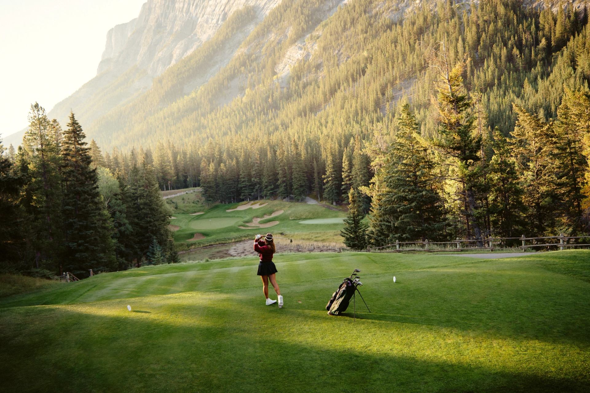 Golfer on a lush fairway at Fairmont Banff Springs Golf Course surrounded by towering pine trees.
