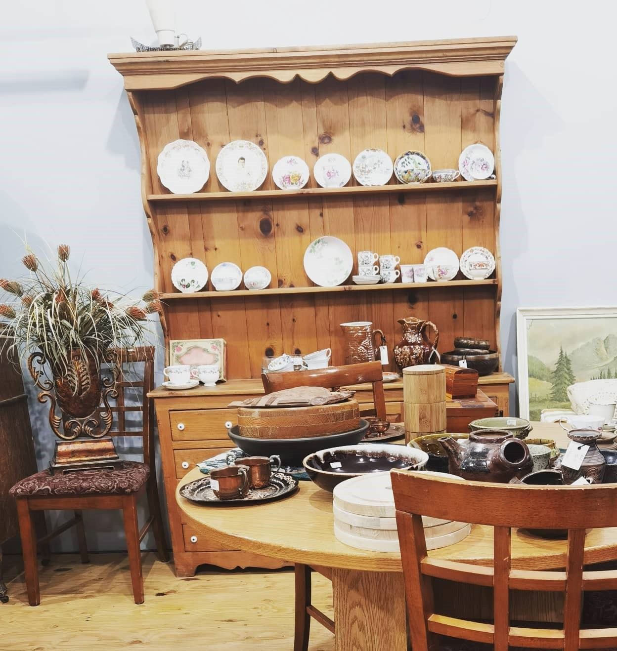 Antique-style table set with teacups, kettle, and shelves of decorative plates in shop display.