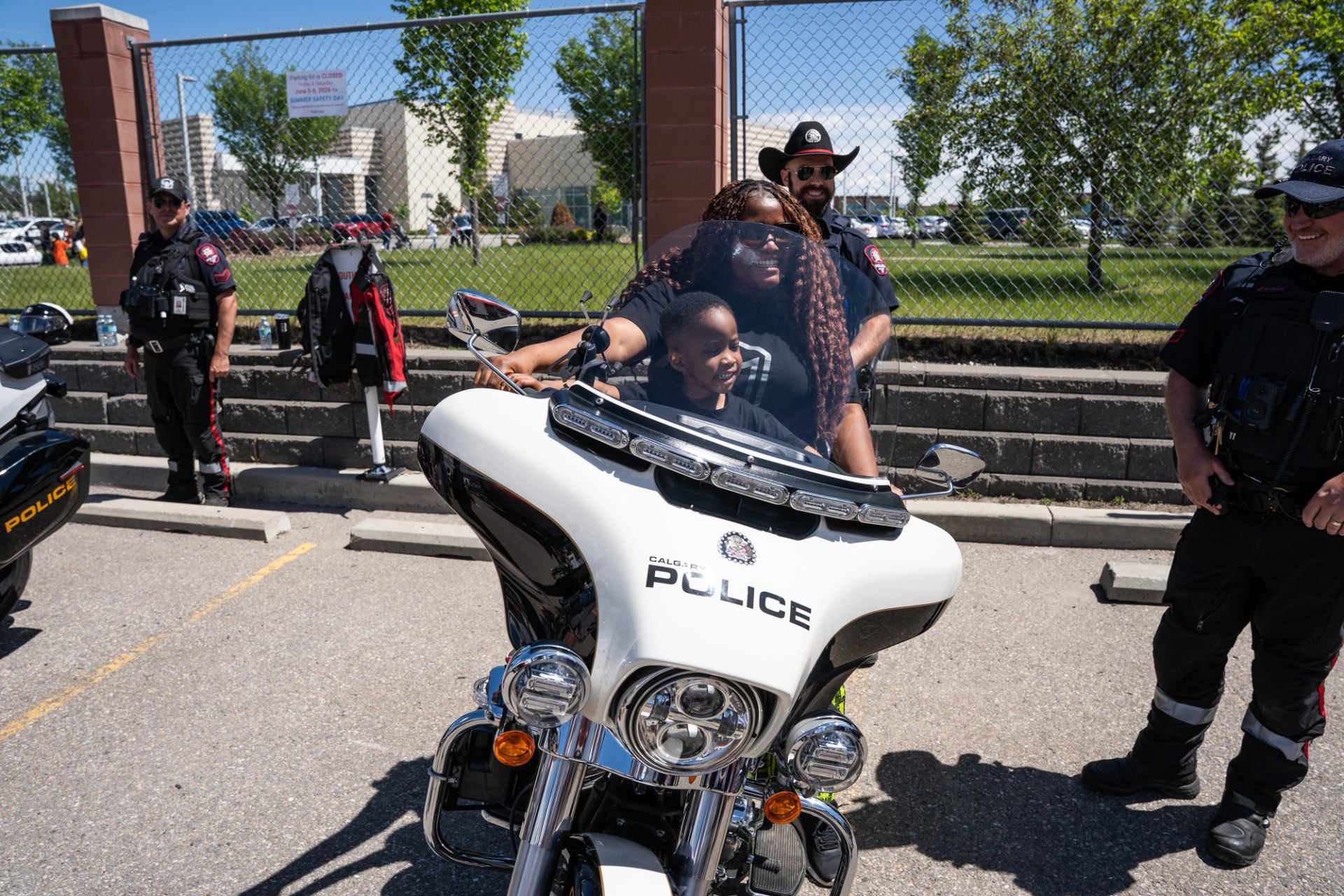 Adult and child sit on a Calgary Police motorcycle surrounded by officers.