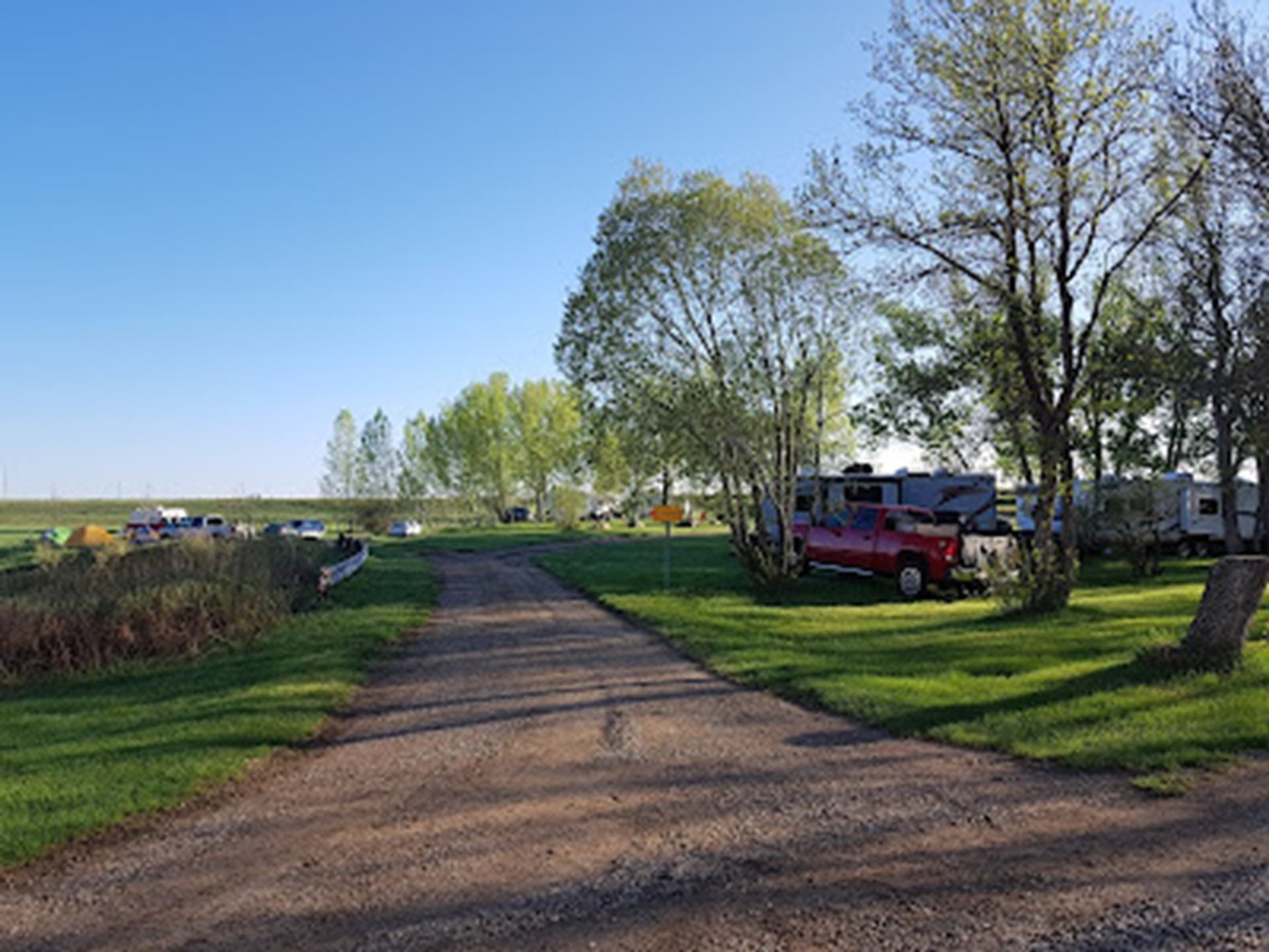 Gravel road through grassy campground with parked RVs, red pickup truck and scattered tents.