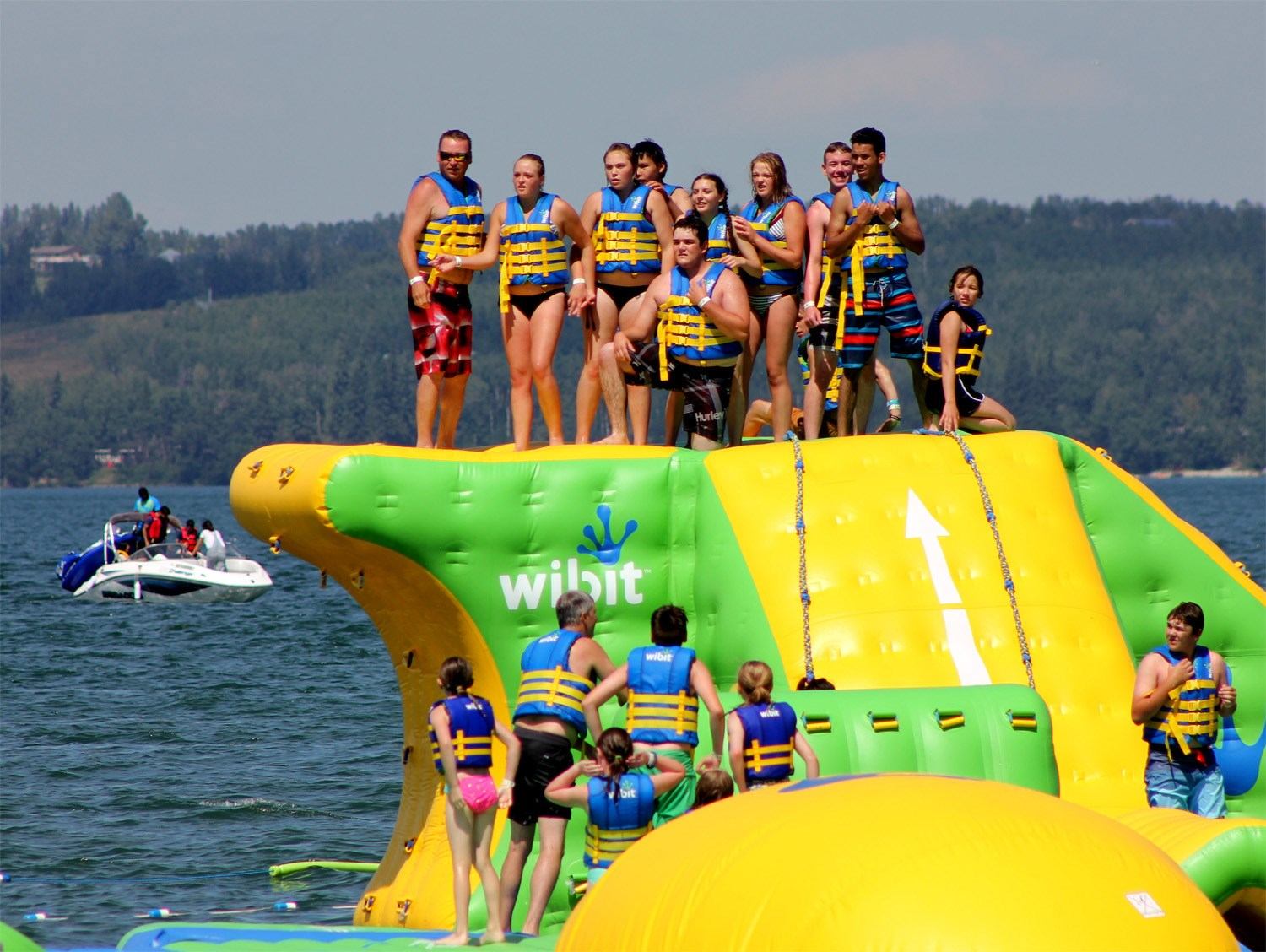 People in life jackets climb and stand on a large inflatable water park structure.