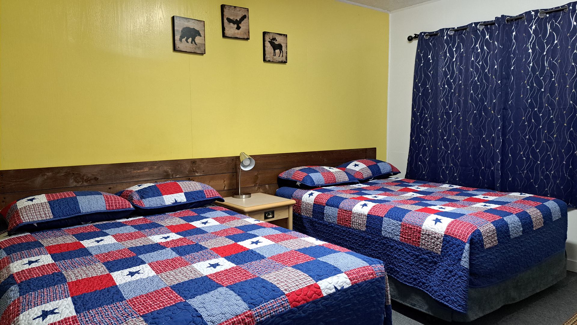 A guest room features two beds with colourful patchwork quilts, bedside lighting, and dark curtains.