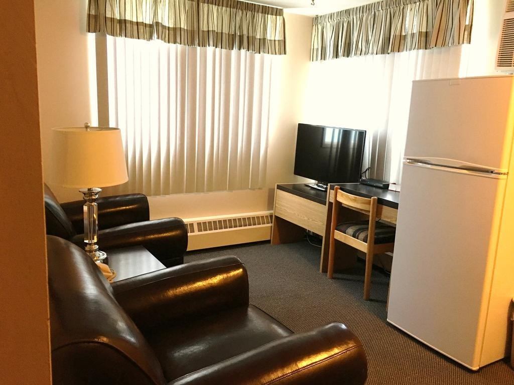 Hotel room with leather armchairs, lamp, TV on stand, and small refrigerator.