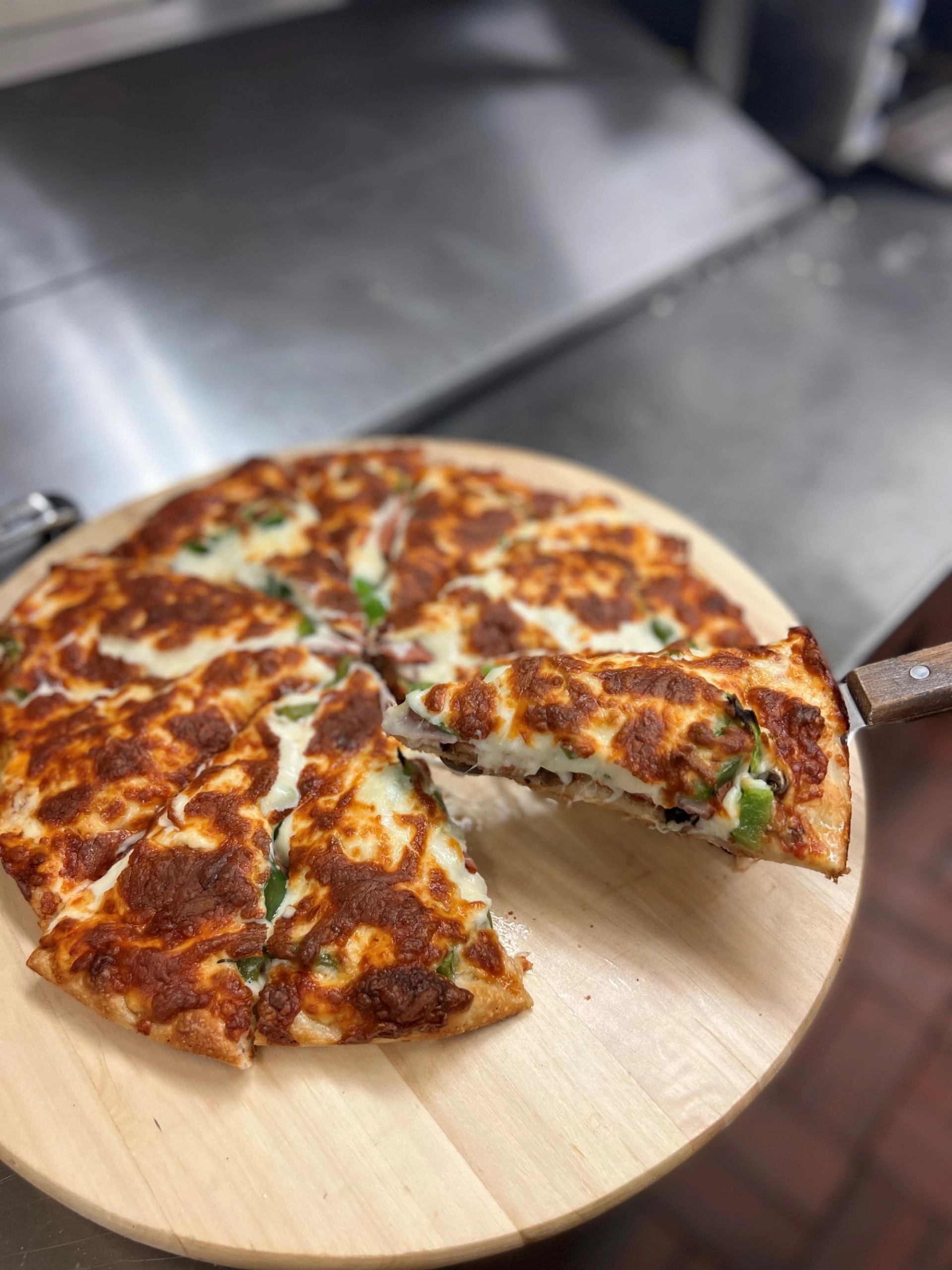 Pizza slices on a wooden board with melted cheese and toppings on an open plate.