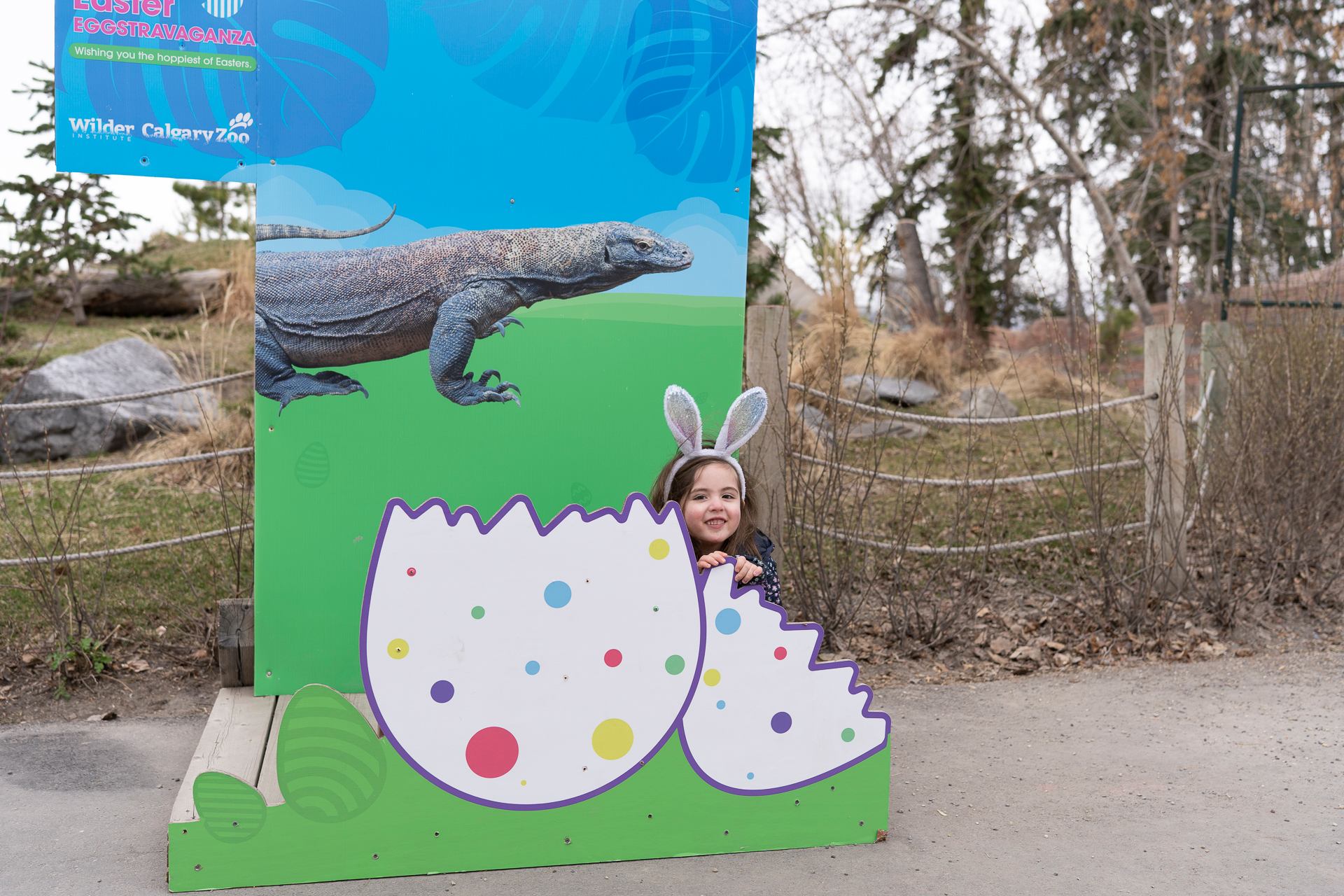 Child wearing bunny ears posing behind a giant cracked Easter egg cutout