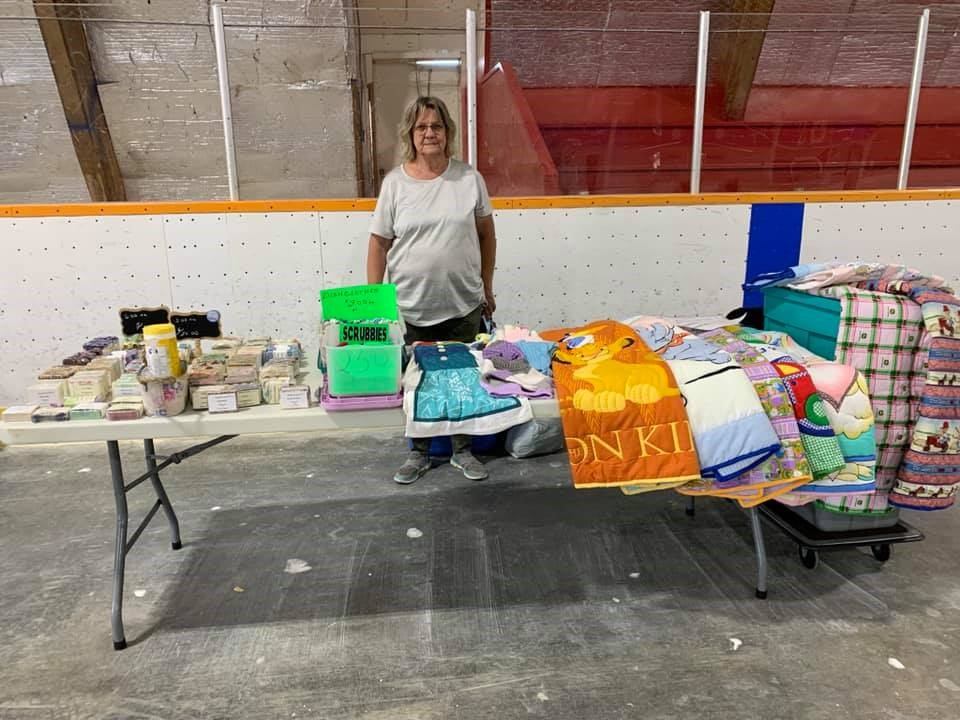 Table with books, boxes, and fabrics at indoor Andrew Farmers' Market event.