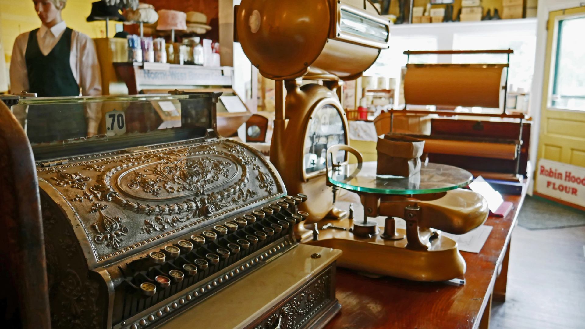 Antique cash register and scale in vintage store with shelves of old-fashioned goods.
