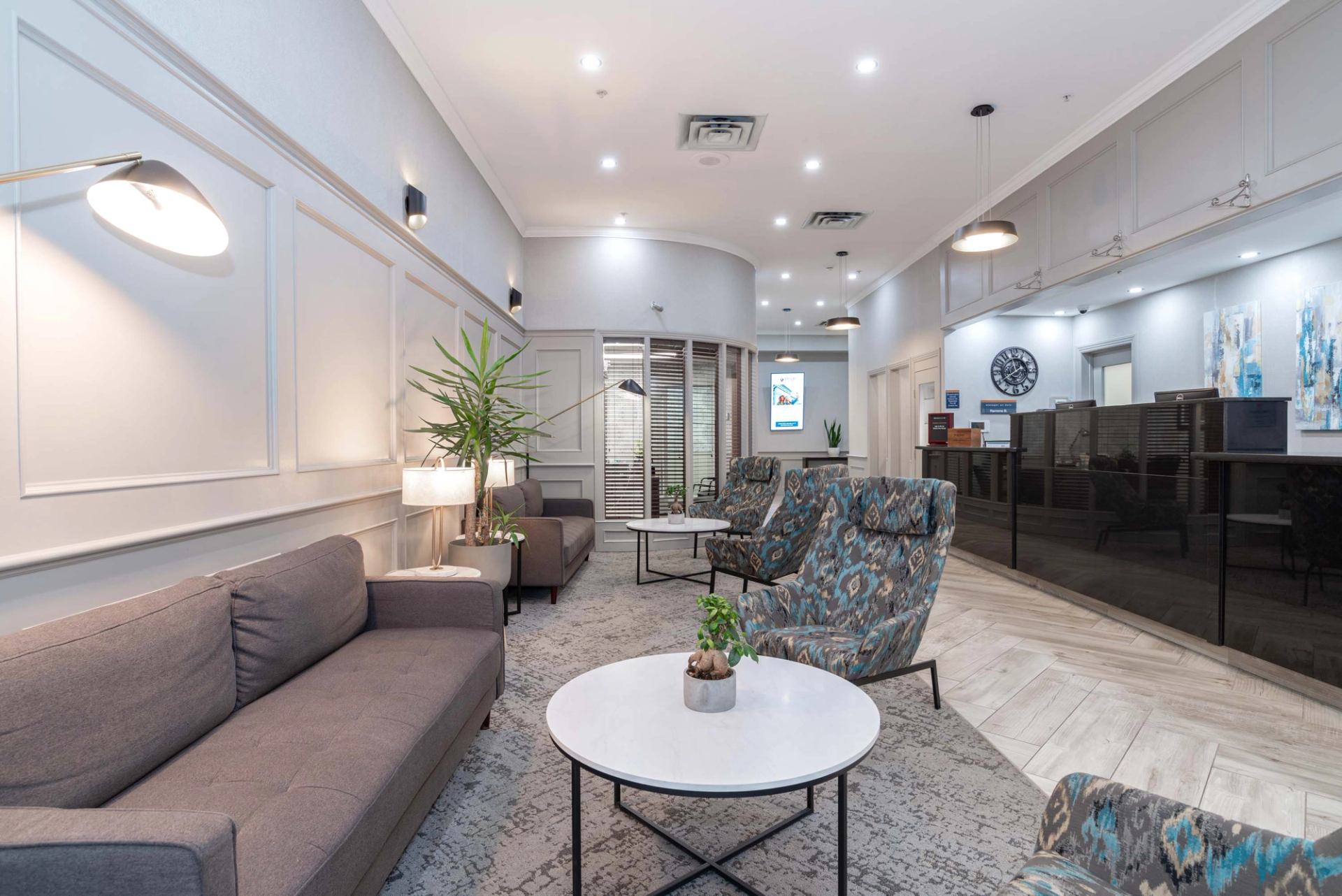 Lobby seating area with sofas, patterned chairs, round tables, plants and reception desk.