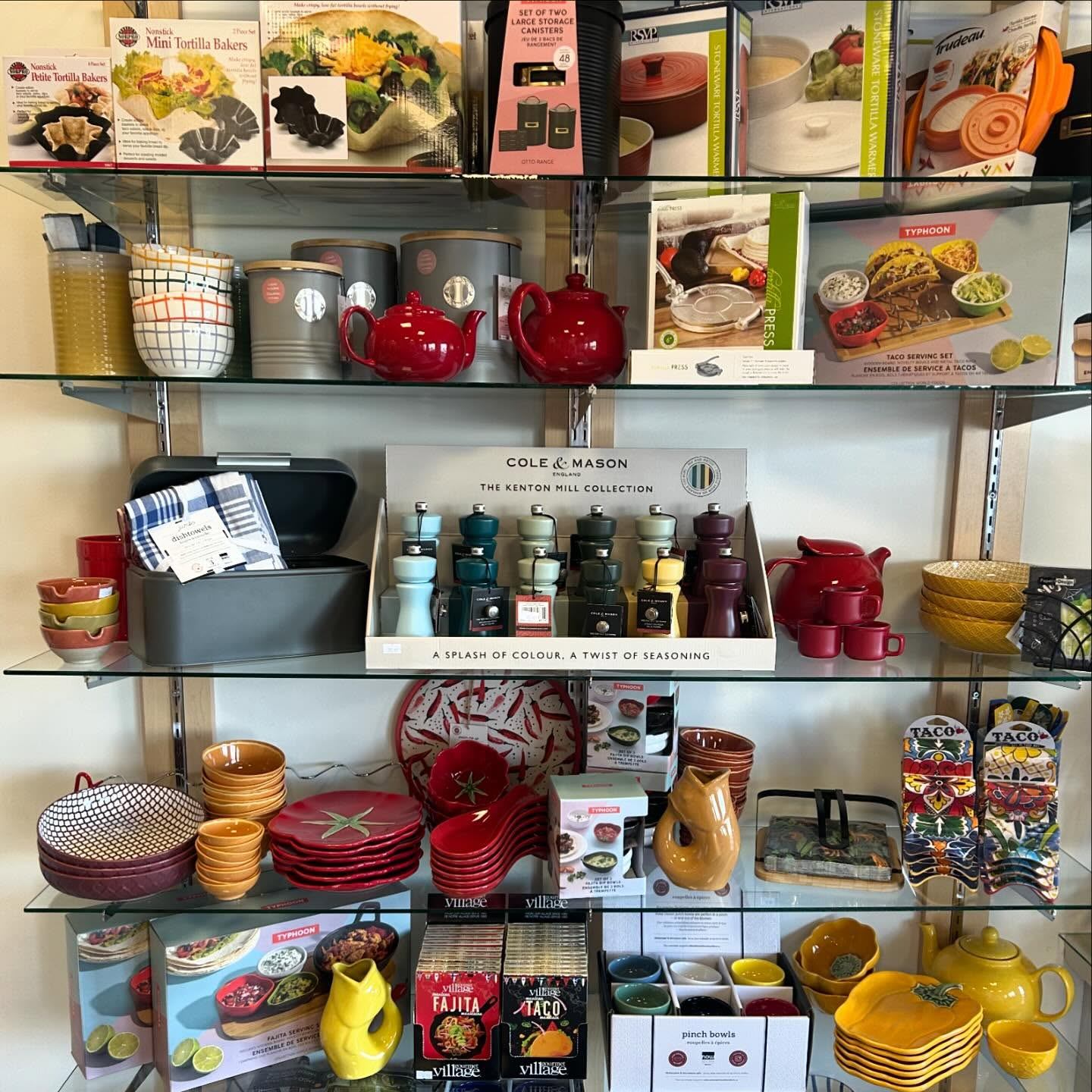 Store shelf displaying colourful kitchenware, spice grinders, taco kits and ceramic bowls.