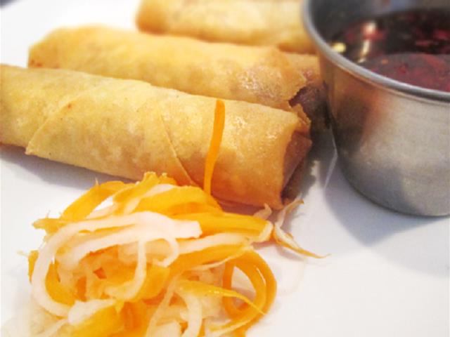 Fried spring rolls with shredded veggies and dipping sauce on a white plate.