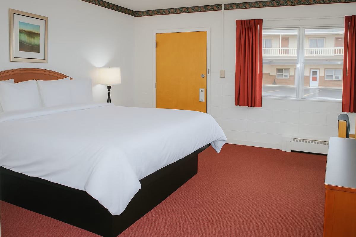 Hotel room with large bed, yellow door, red curtains and window facing exterior walkway.