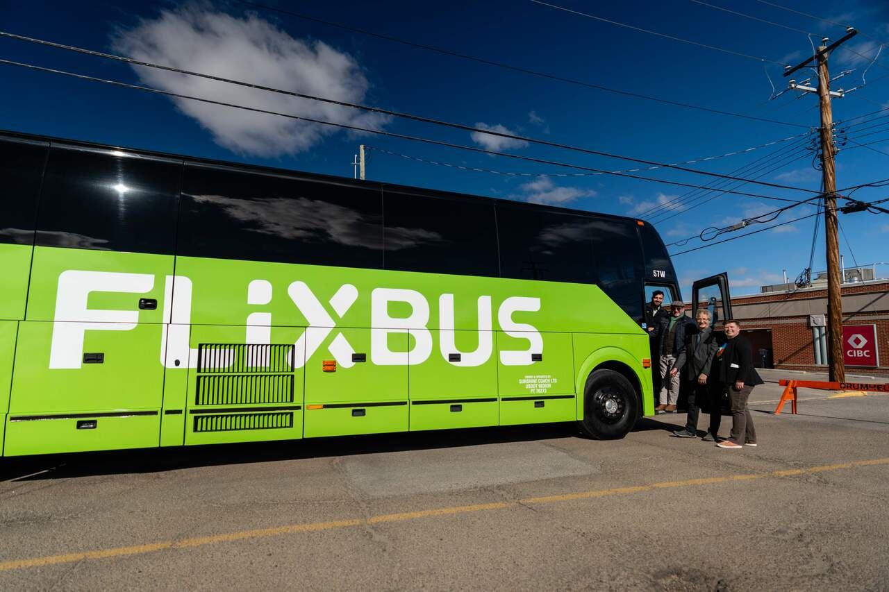 Green FlixBus coach parked on street with four people standing near open door.