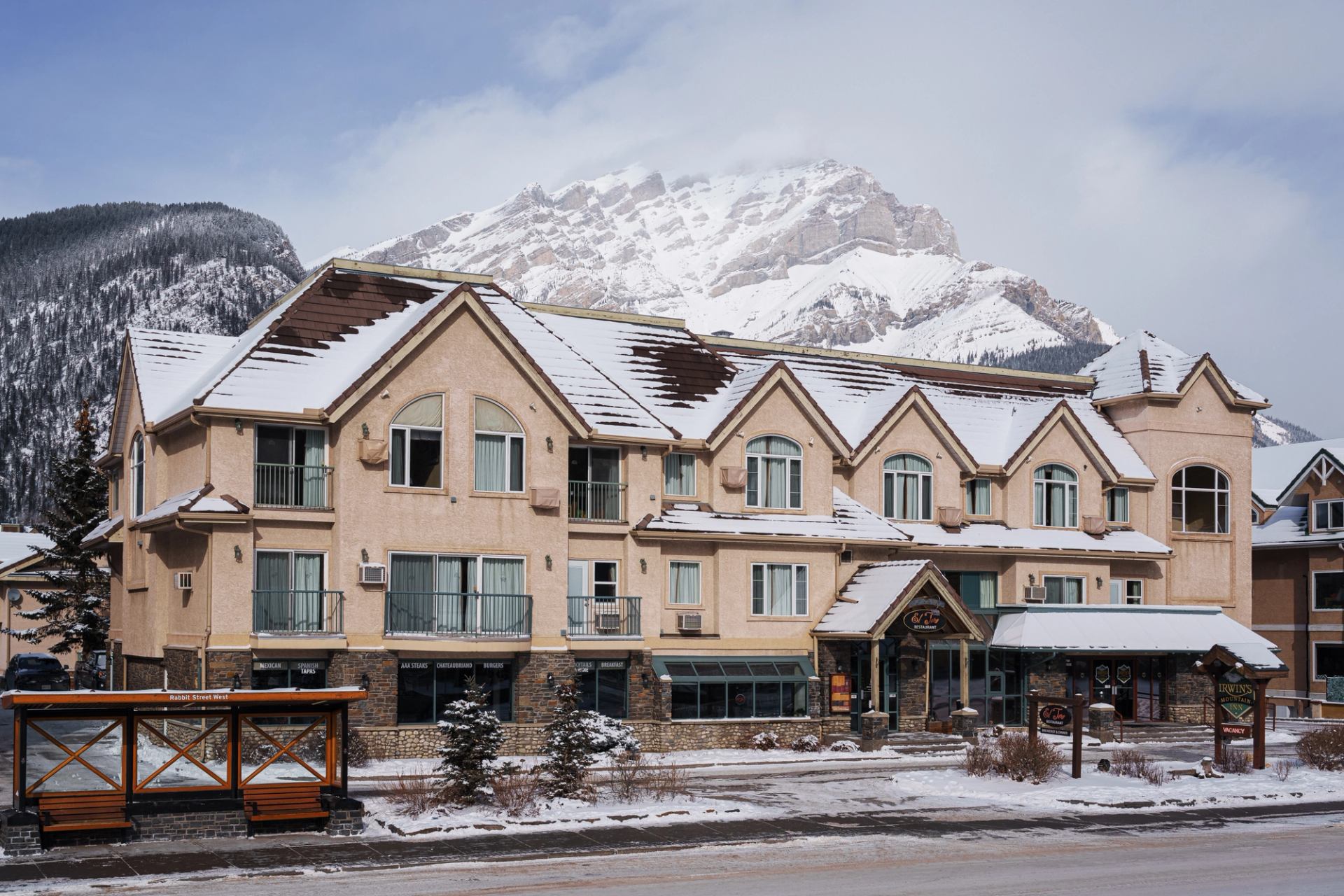 Lodge-style hotel with snowy mountain backdrop and clear blue sky.