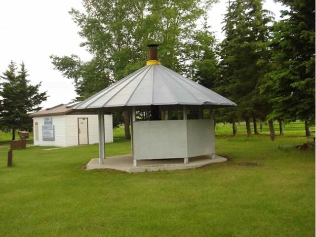 Campground shelter with metal roof, white building, and grass lawn in park.
