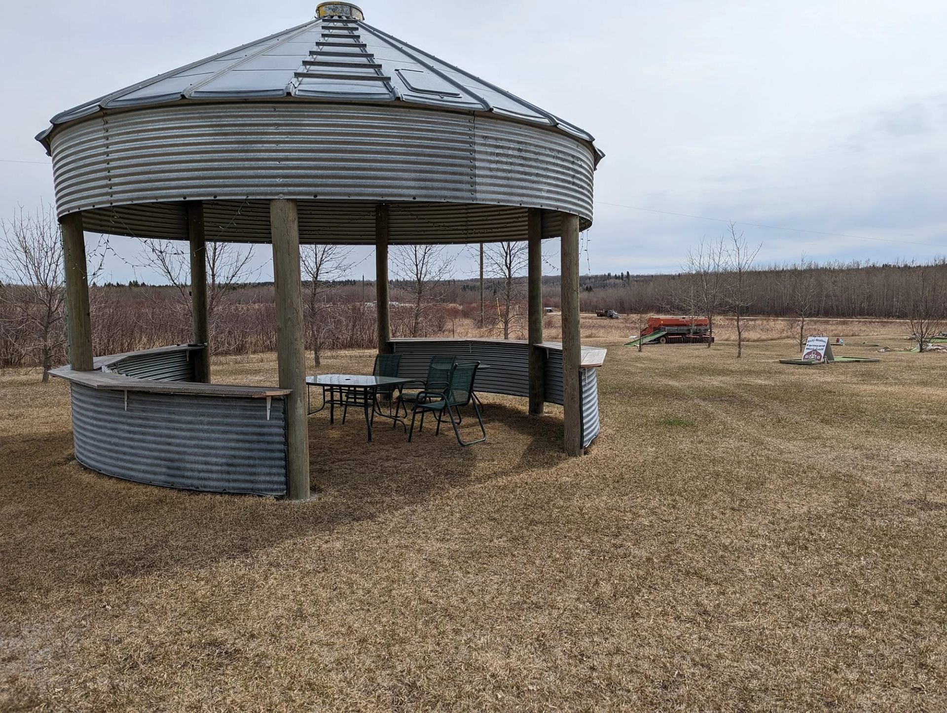 Metal gazebo made from grain bin with patio table on dry grassy field.