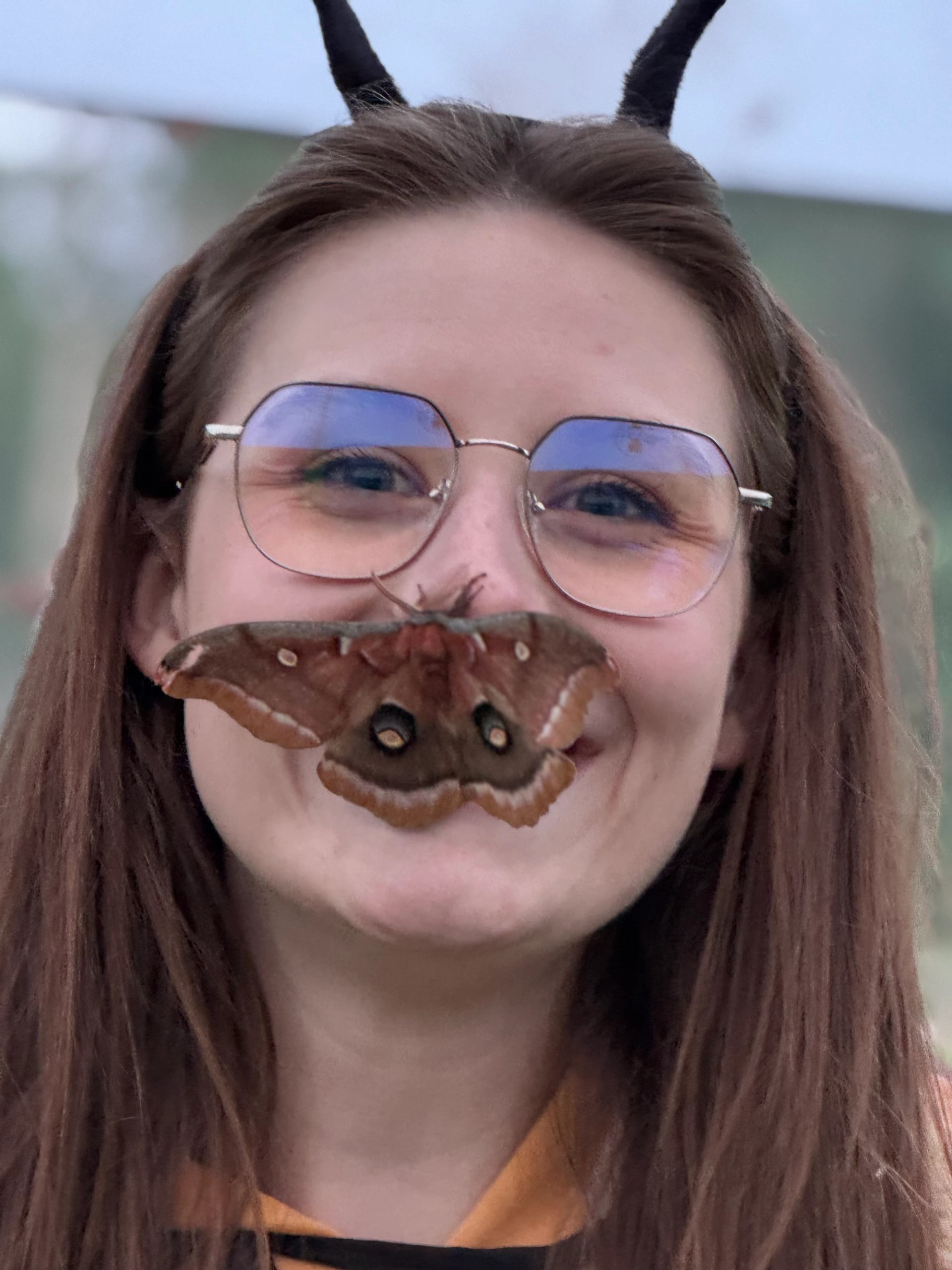Large brown moth rests on person’s face, covering mouth and nose, near glasses.