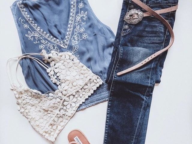 Clothing display with denim jeans, blue embroidered top, and white lace bra in foreground.