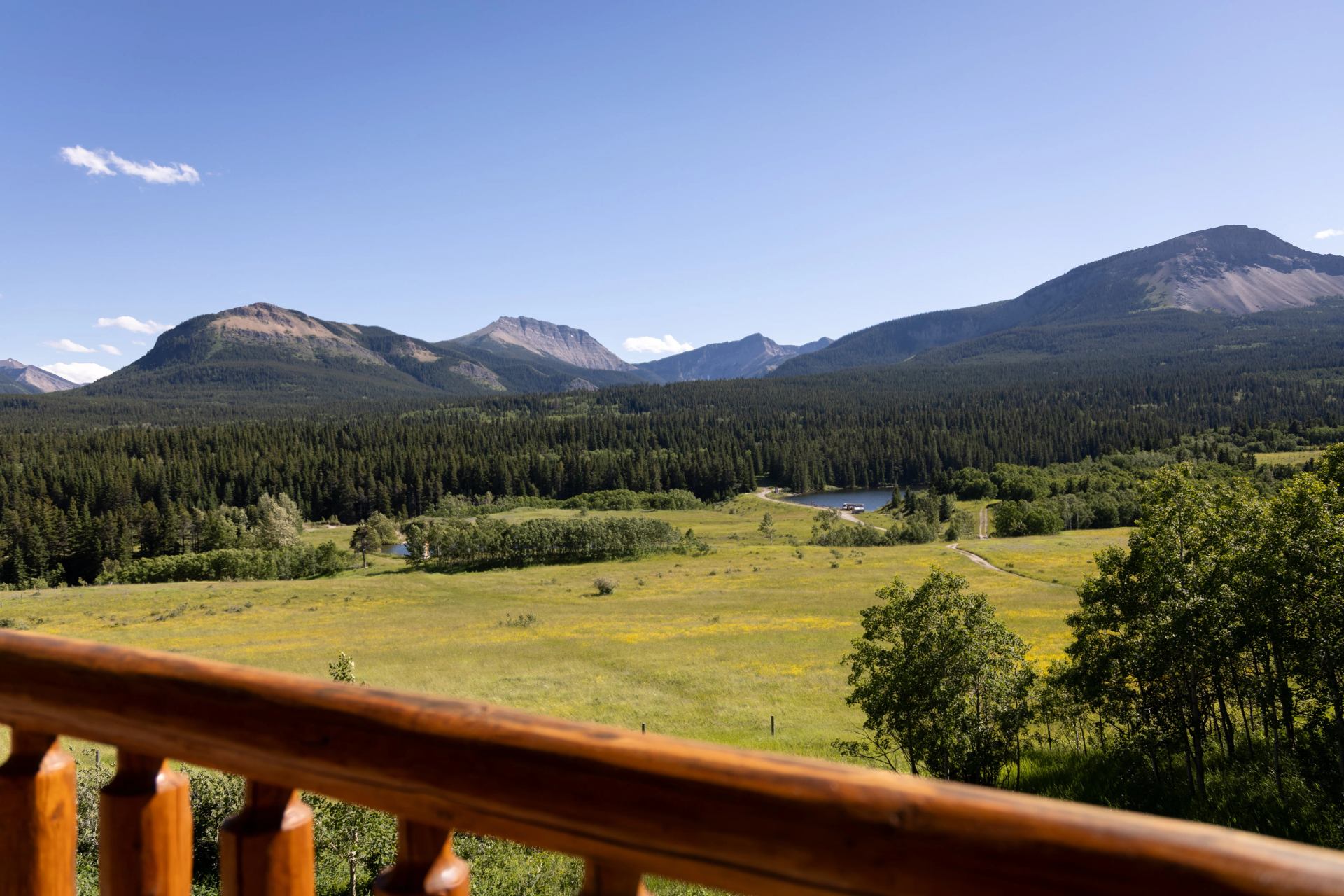 Forested mountains, open meadows and a pond viewed from the ranch balcony.