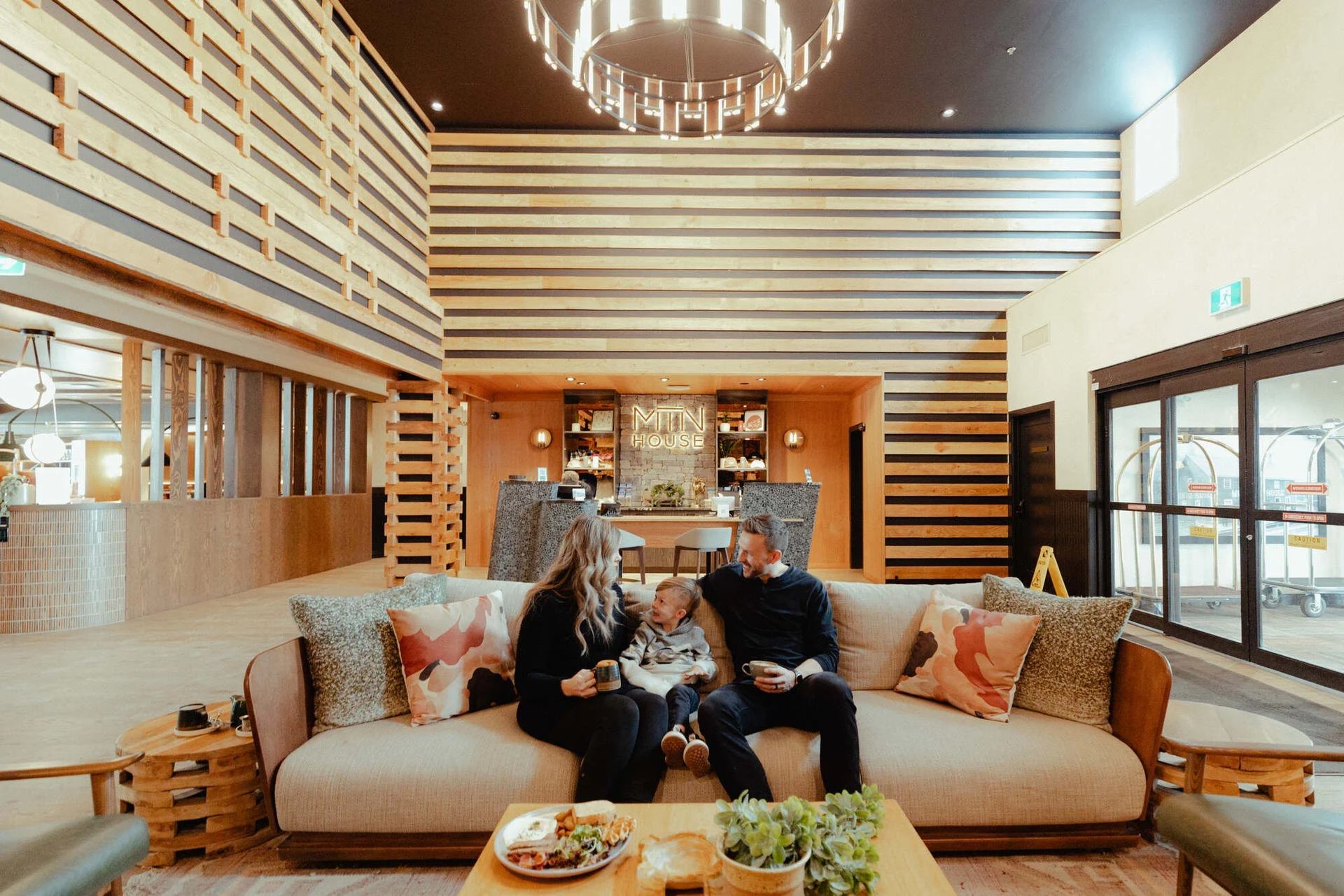 Family relaxing on a couch in a modern lodge lobby with wood paneling.