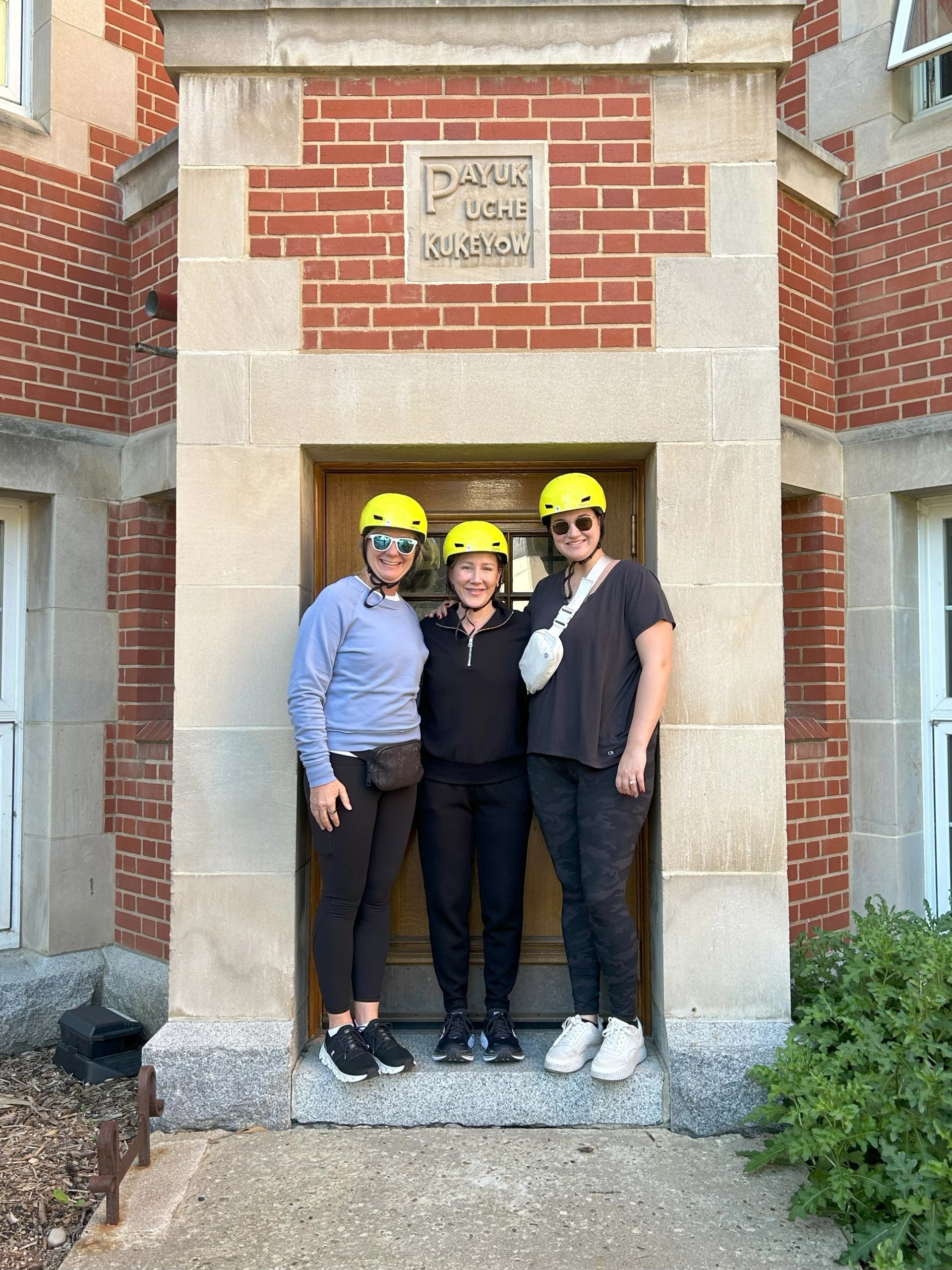 Two people in yellow helmets pose with bike on bridge, city skyline in background.