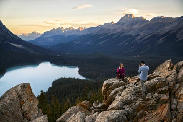 A couple take pictures while sitting on the rocks overlooking Peyto Lake.