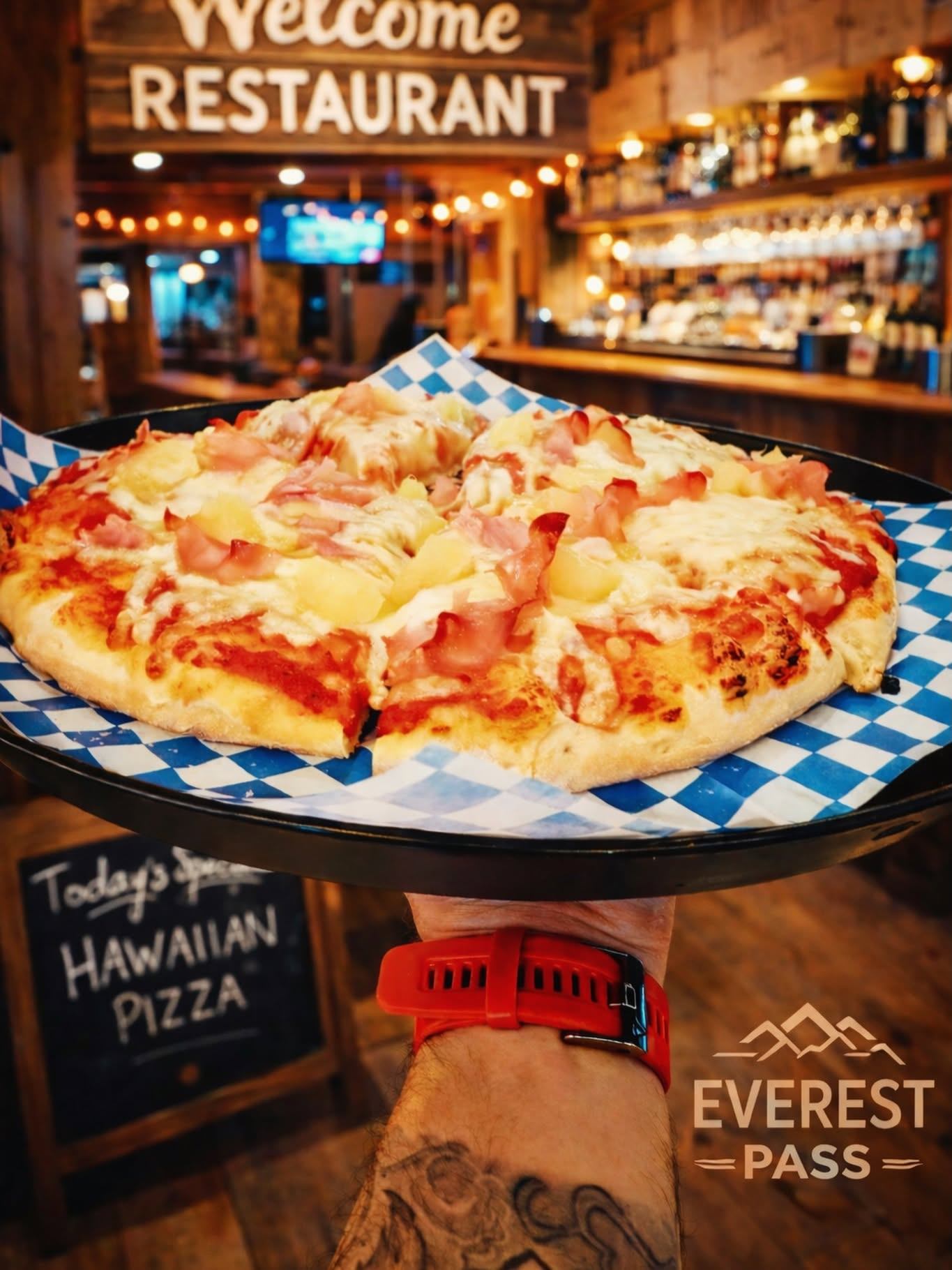 A Hawaiian pizza topped with ham, pineapple, and melted cheese is served in a cozy pub setting.