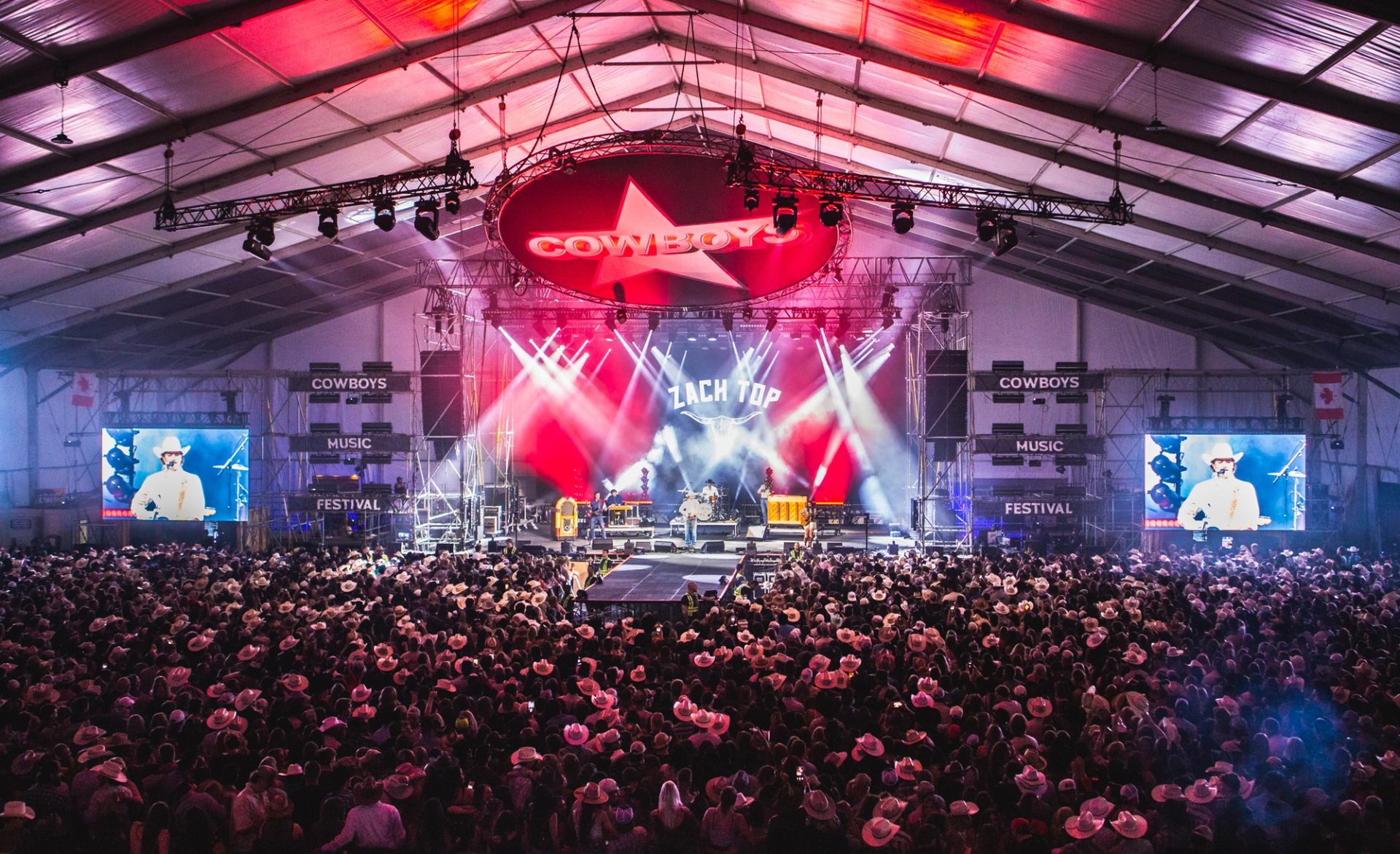 Wide view of a crowded festival tent with a brightly lit stage at Cowboys Music Festival.