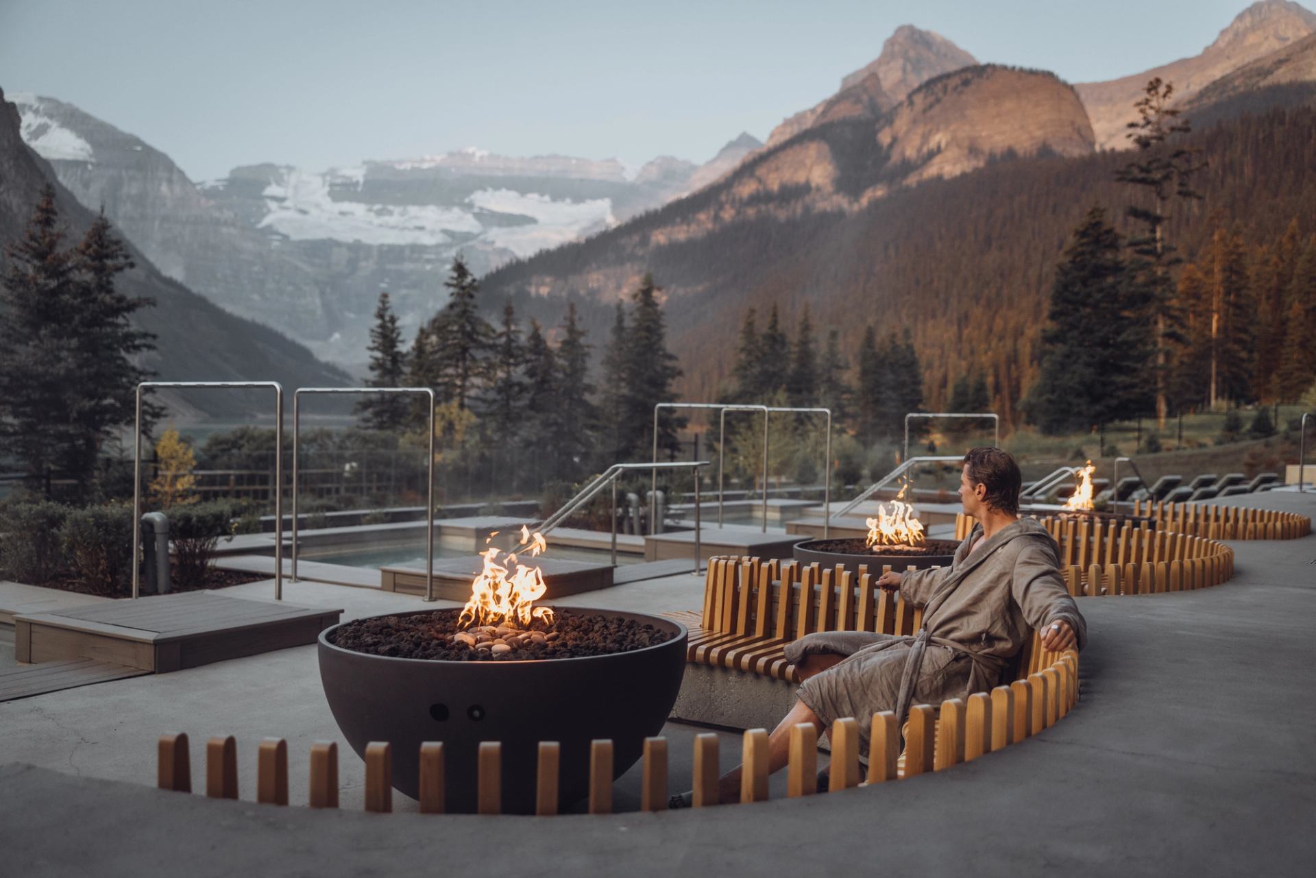 A man sits on a deck near a fire pit overlooking the Canadian Rockies.