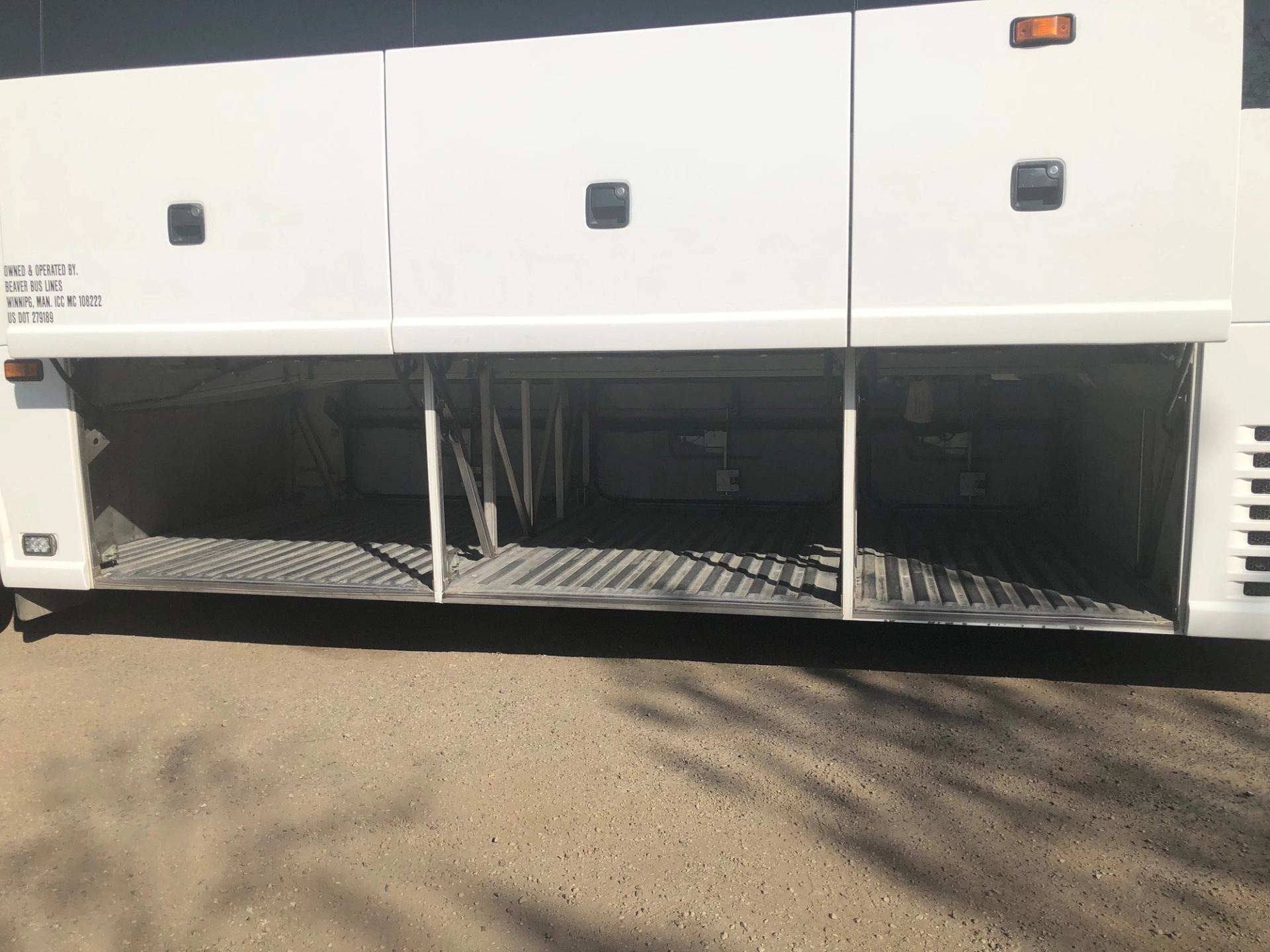 White bus with open luggage compartments showing empty storage space.