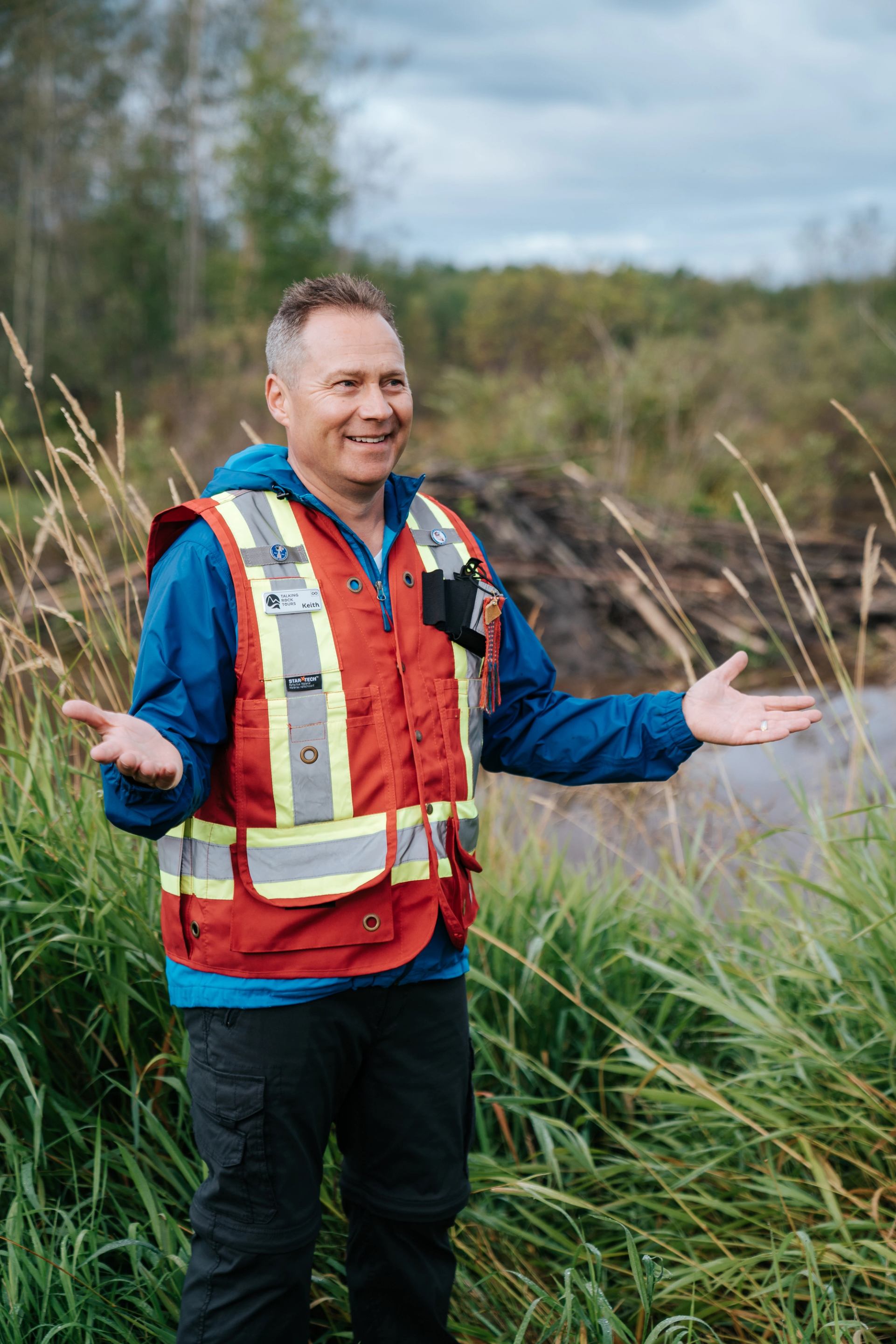 A Métis guide in a survey vest stands near a beaver lodge.