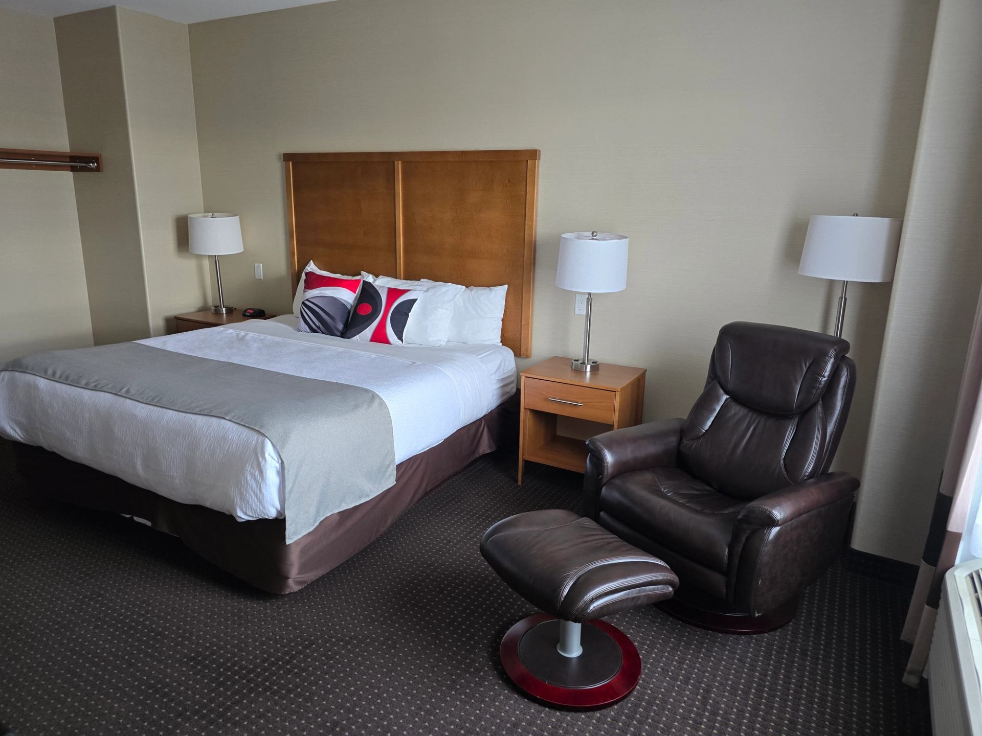 Hotel room with double bed, bedside tables, table lamps, and black leather armchair.