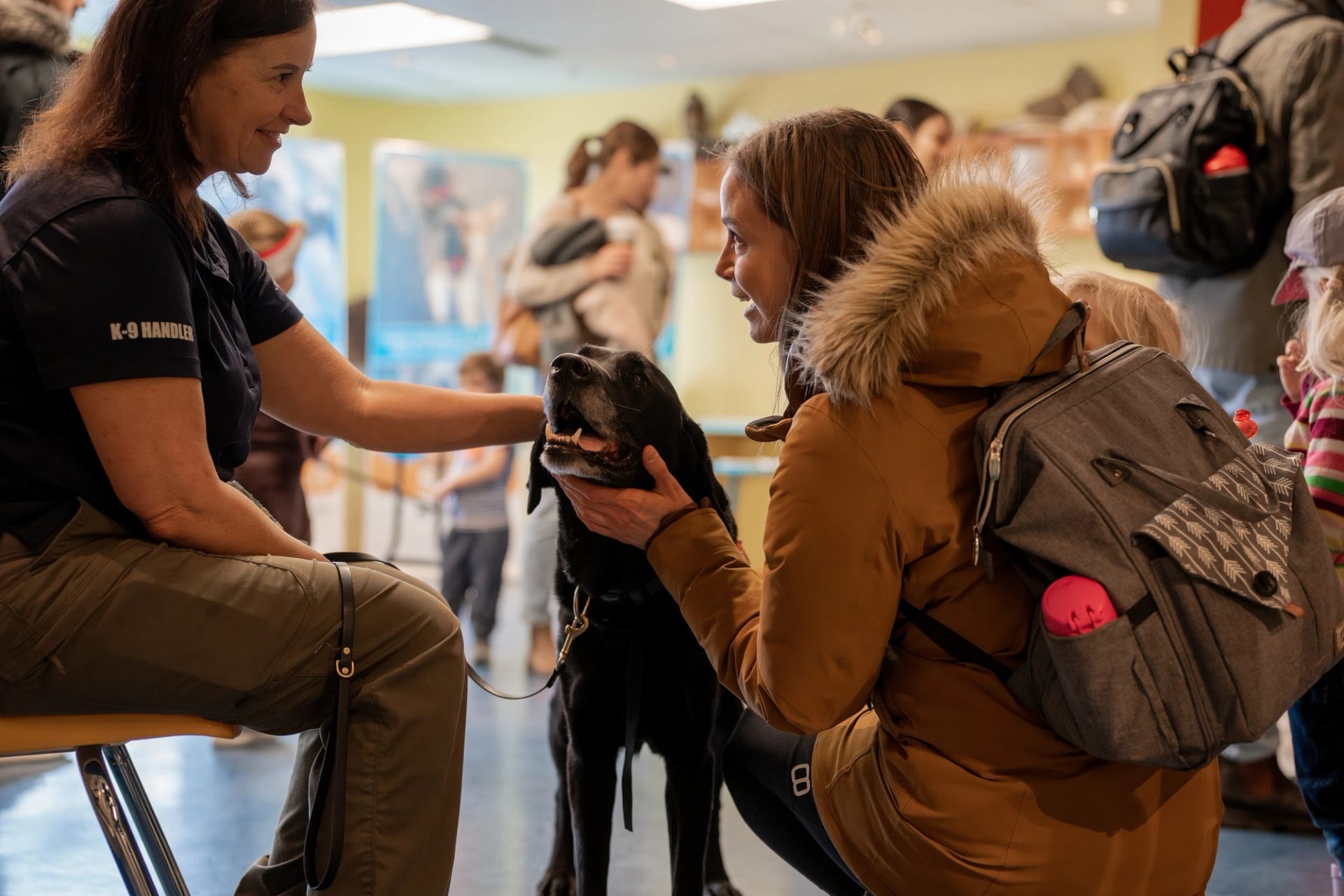 Person kneeling to pet a black dog at an indoor Fishtival event with others in the background.