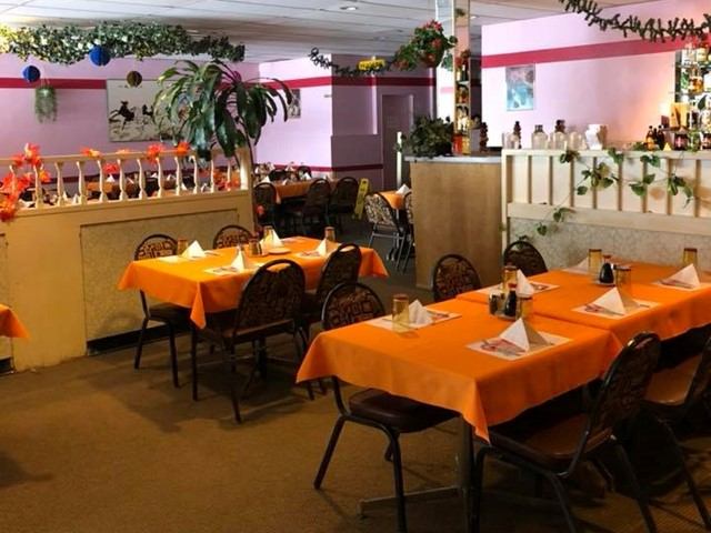 Dining room features orange tablecloths, neatly set tables, decorative plants, and buffet-style seating.