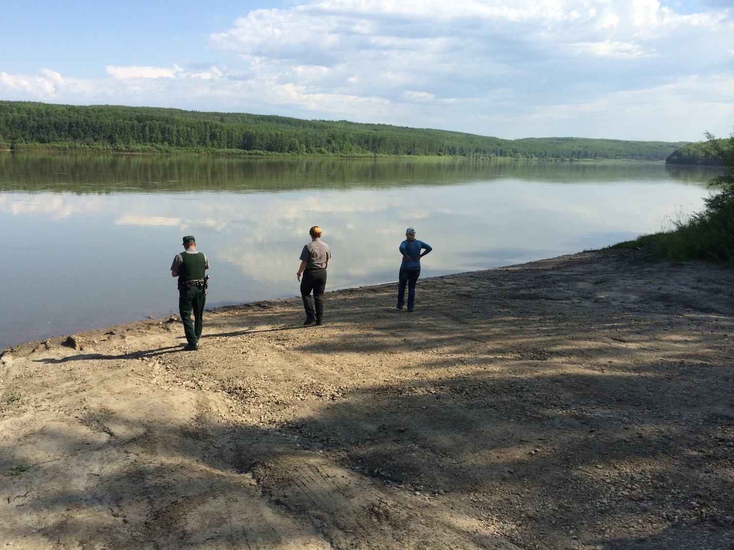 Three people standing on the sandy bank of the Athabasca River facing the water