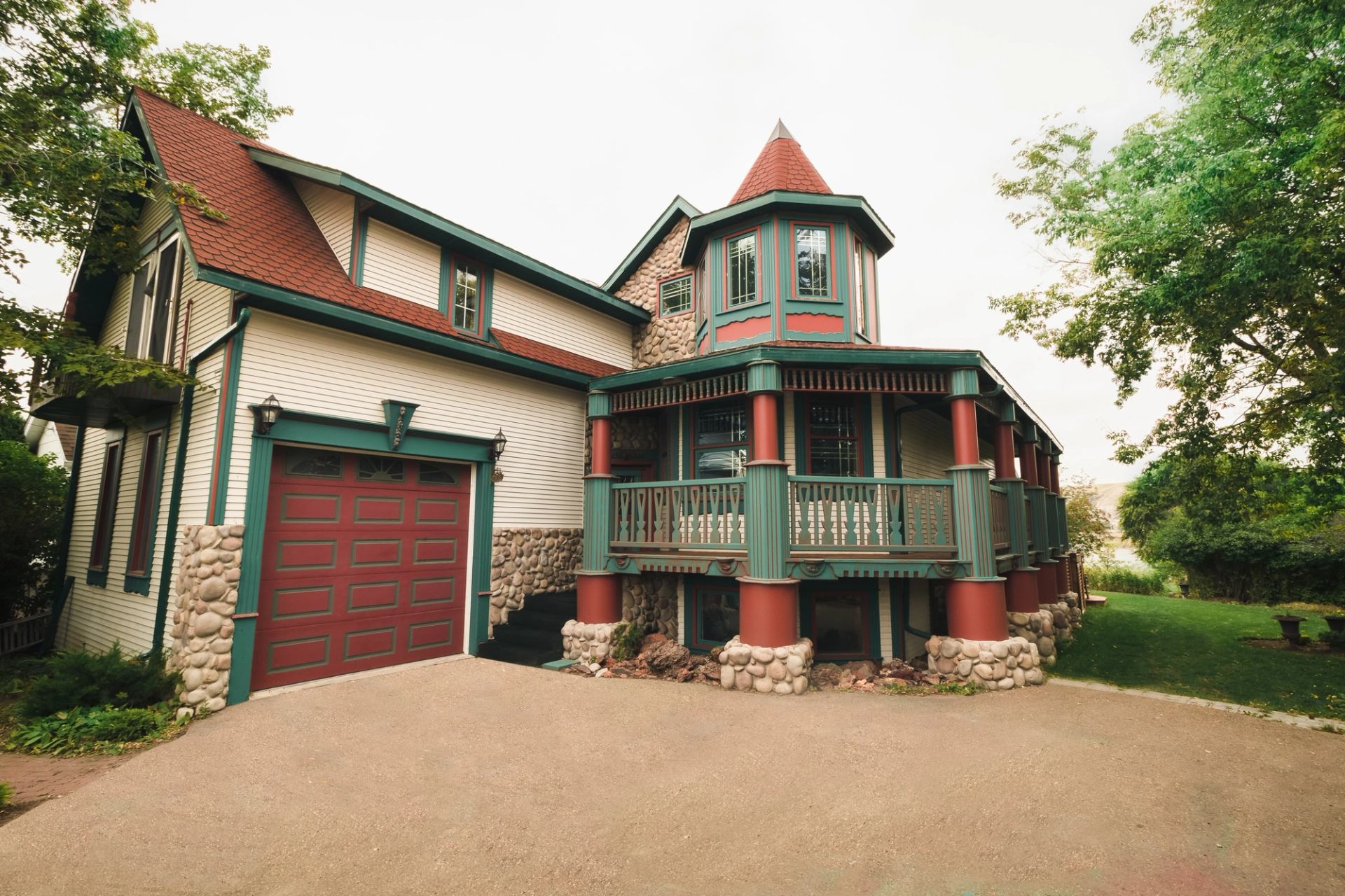 Charming stone-and-wood cottage with red roof and green trim surrounded by trees.