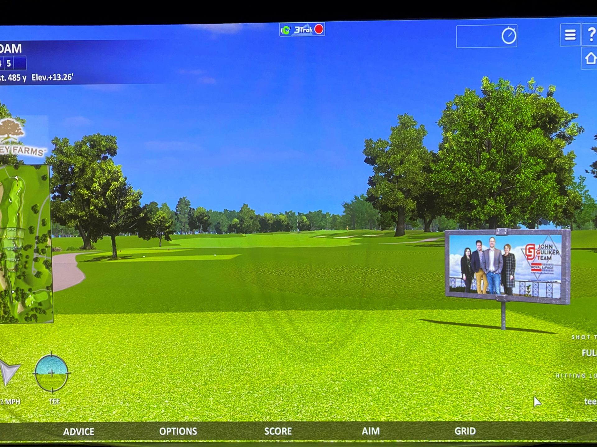 Golf simulator screen showing virtual fairway, trees, course map and on-screen controls.