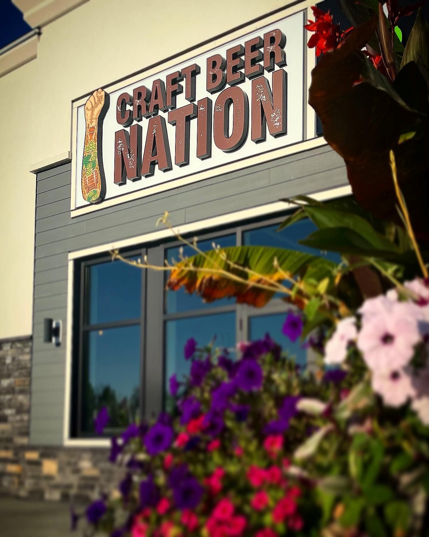 Craft Beer Nation storefront with sign, flowers, and modern stone-wood exterior.