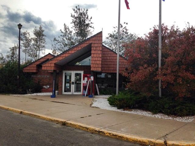 Small building with triangular roof, flags, and trees with autumn foliage.