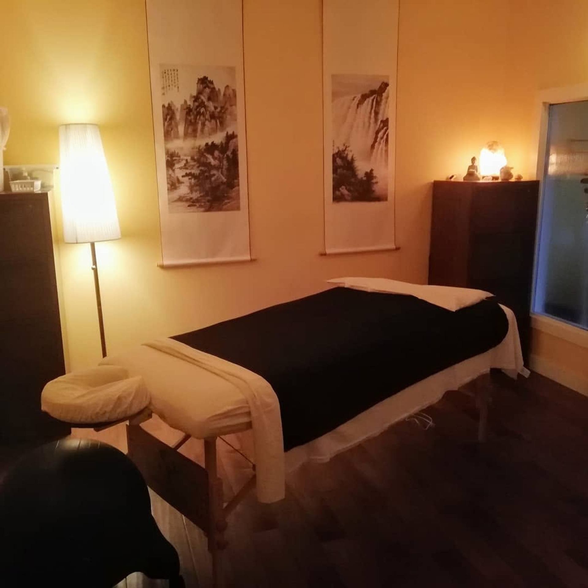 A tranquil massage room features a treatment table, warm lighting, artwork, and calming décor.