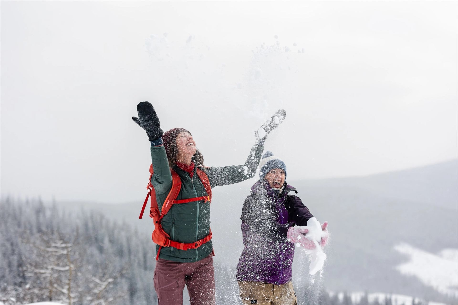 Two people toss snow into the air on a snowy mountain ridge at Athabasca Lookout.