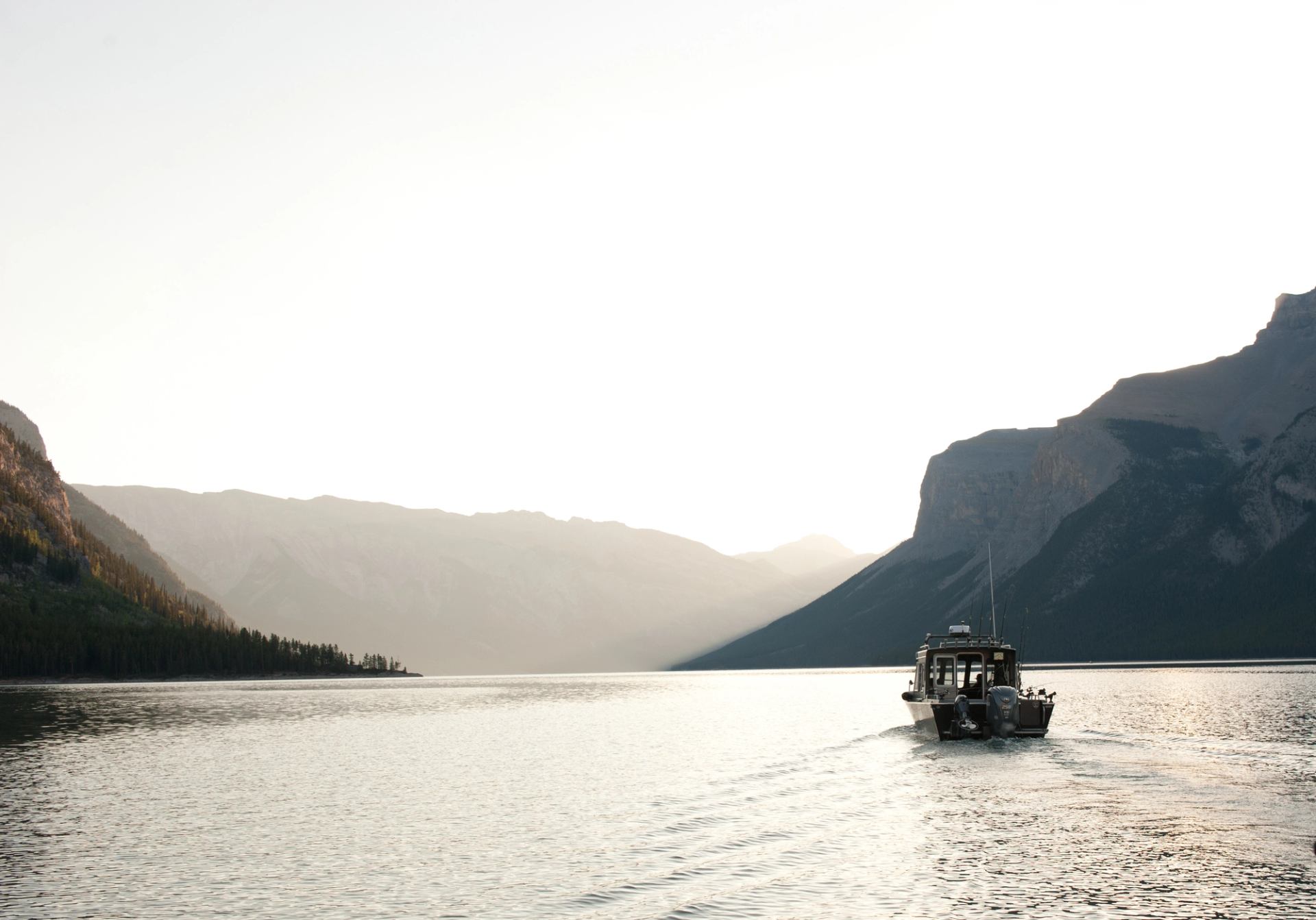 Boat moving across a still lake with mountains rising in the soft evening light.