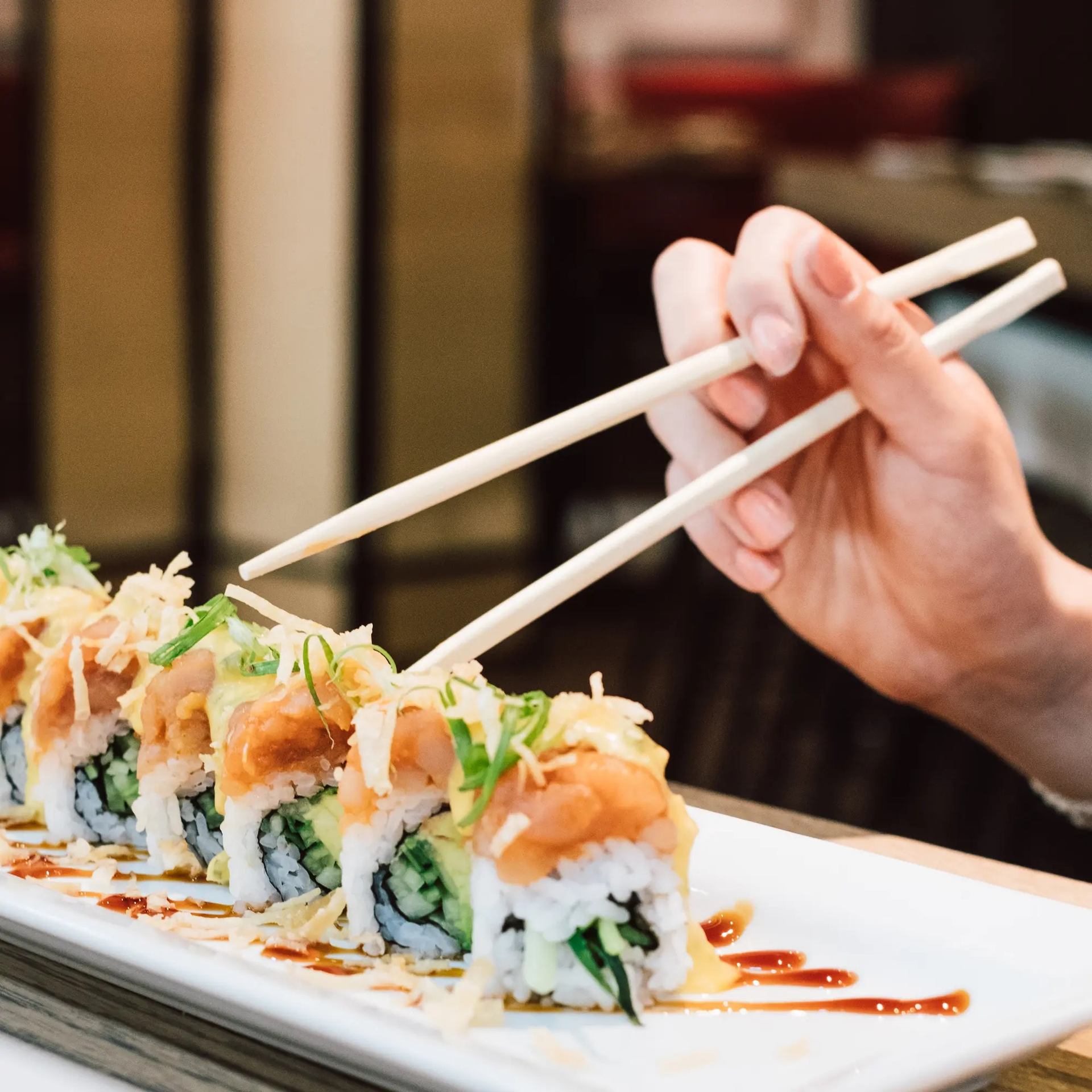 Hand with chopsticks picking sushi from garnished plate.