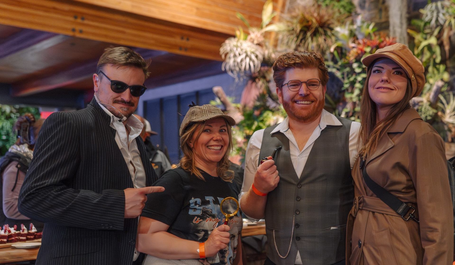 Costumed group poses with a magnifying glass and smoking pipes indoors.