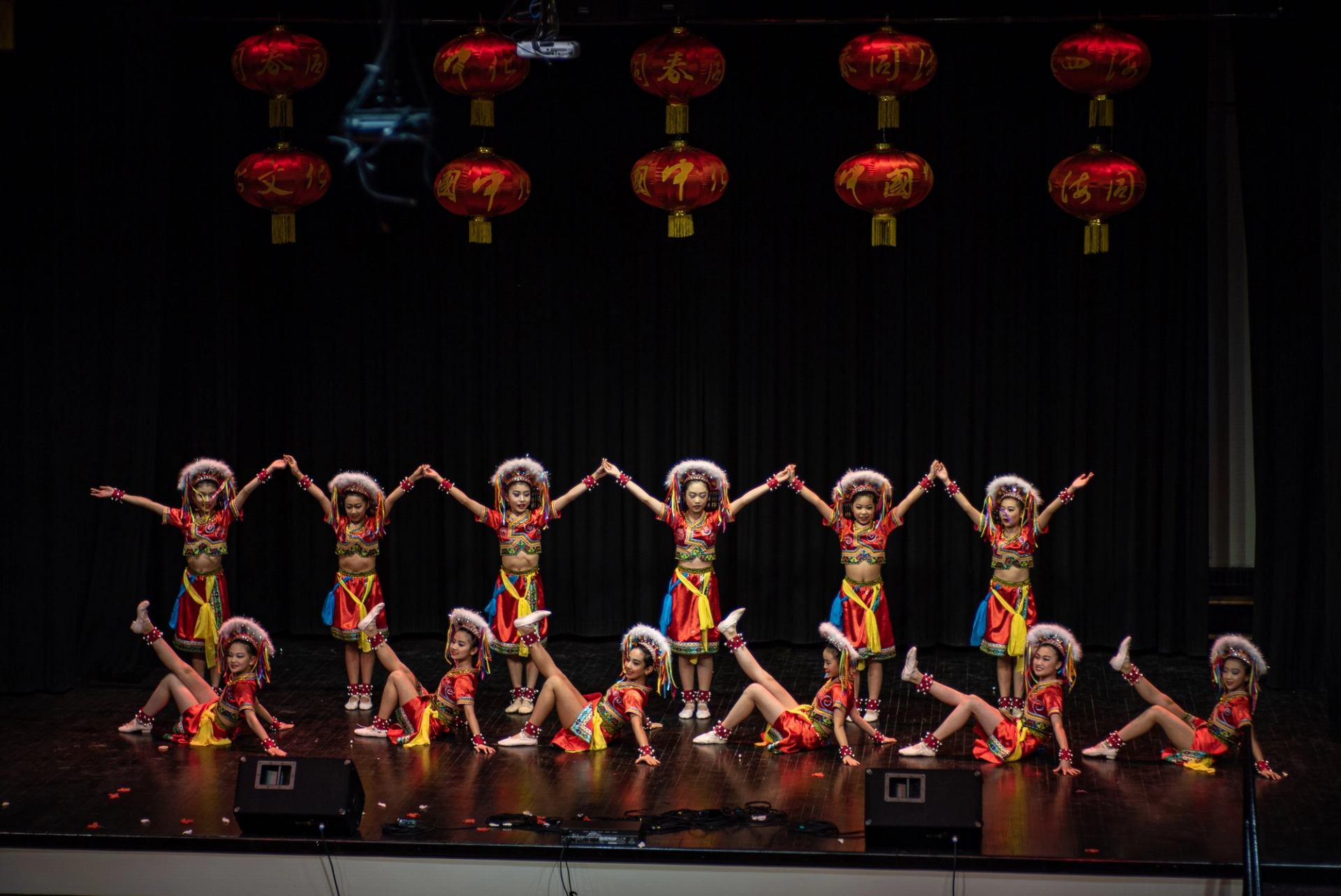 Group of dancers in colorful costumes performing a synchronized routine under red lanterns.