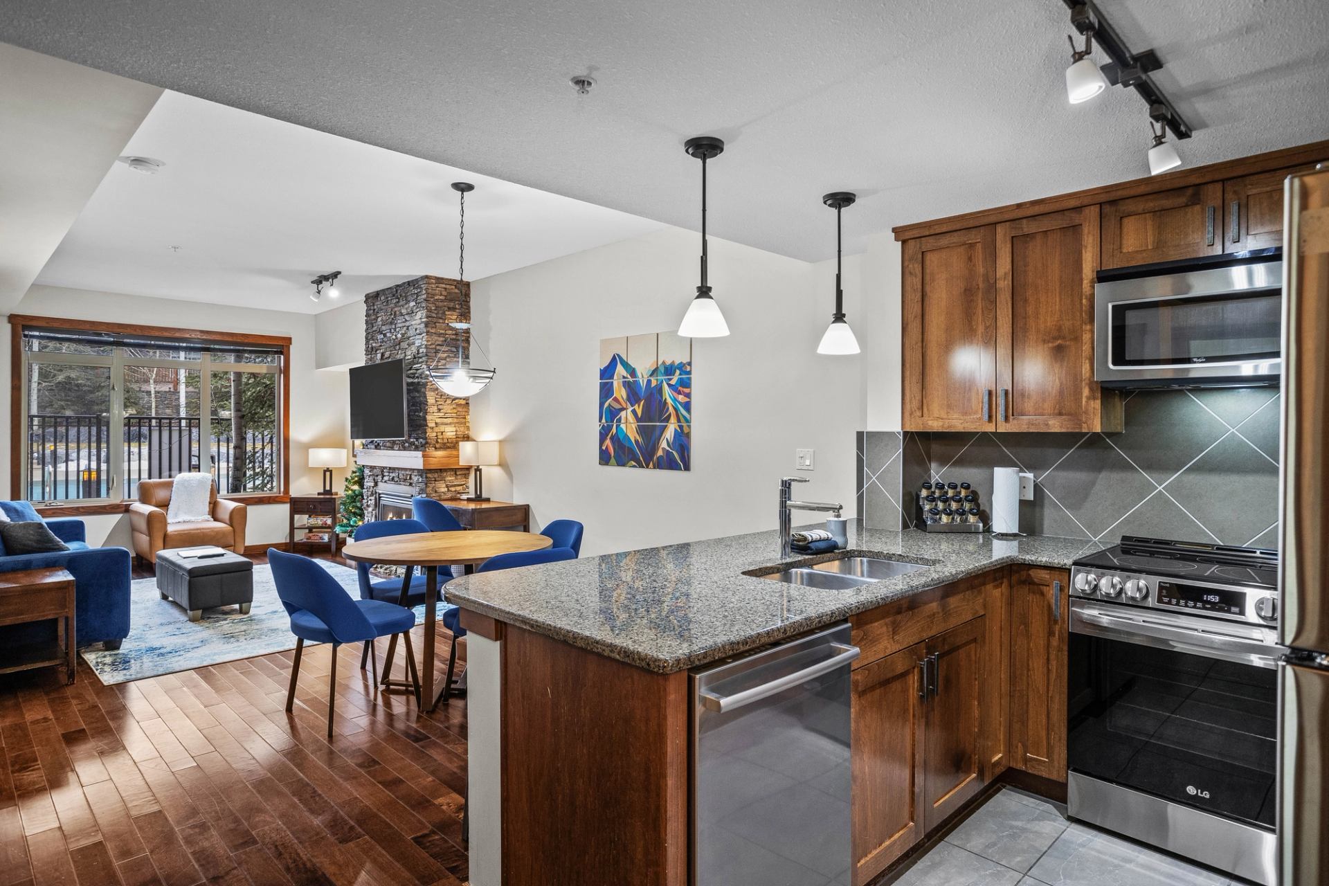 Open-concept kitchen and living room with stone fireplace, blue chairs and large window.