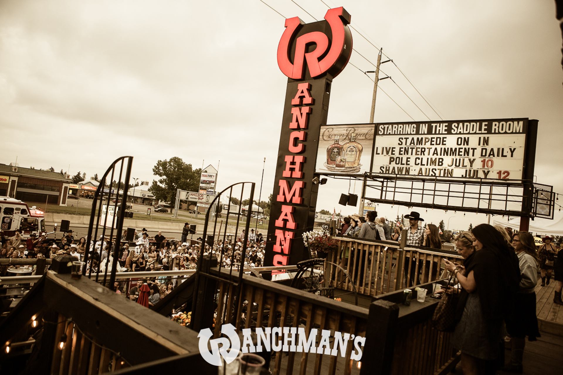 Outdoor crowd at Ranchman’s patio beneath large neon sign and Saddle Room event marquee.